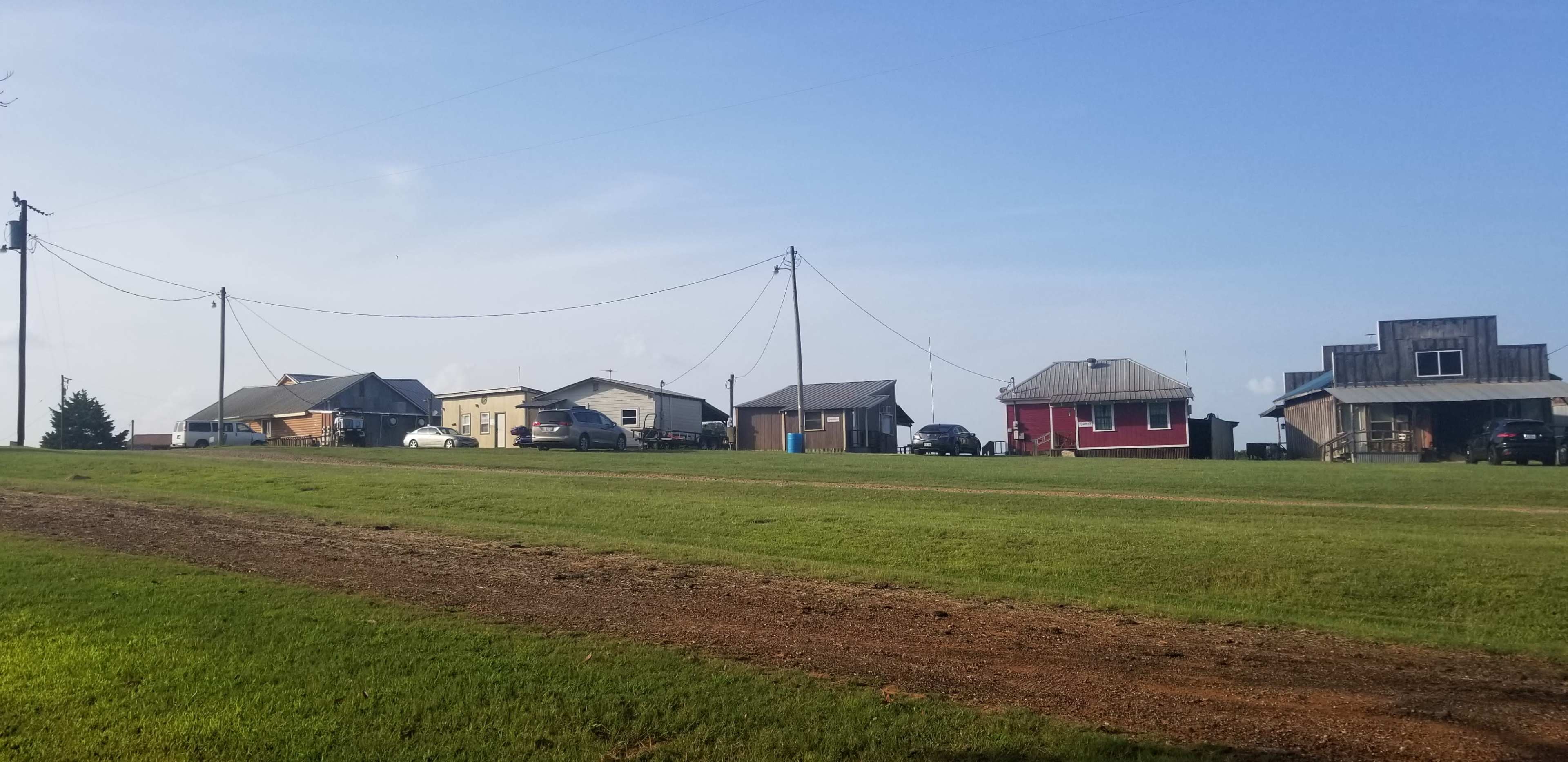 A row of houses line a grassy hillside under a clear blue sky, with utility poles and wires extending along the property.