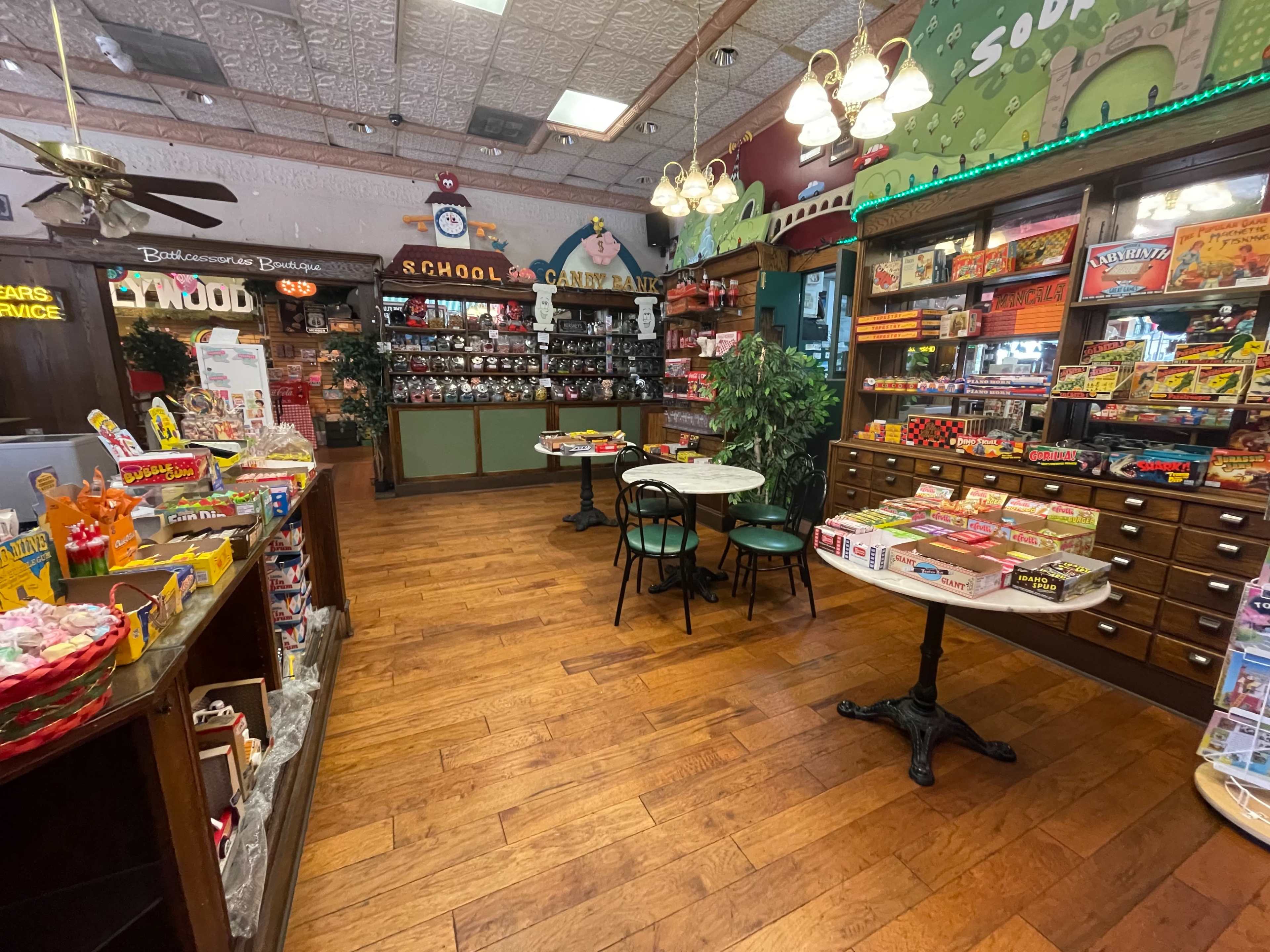 The interior of a nostalgic candy shop features wooden floors, shelves filled with colorful candies, and tables set with chairs.