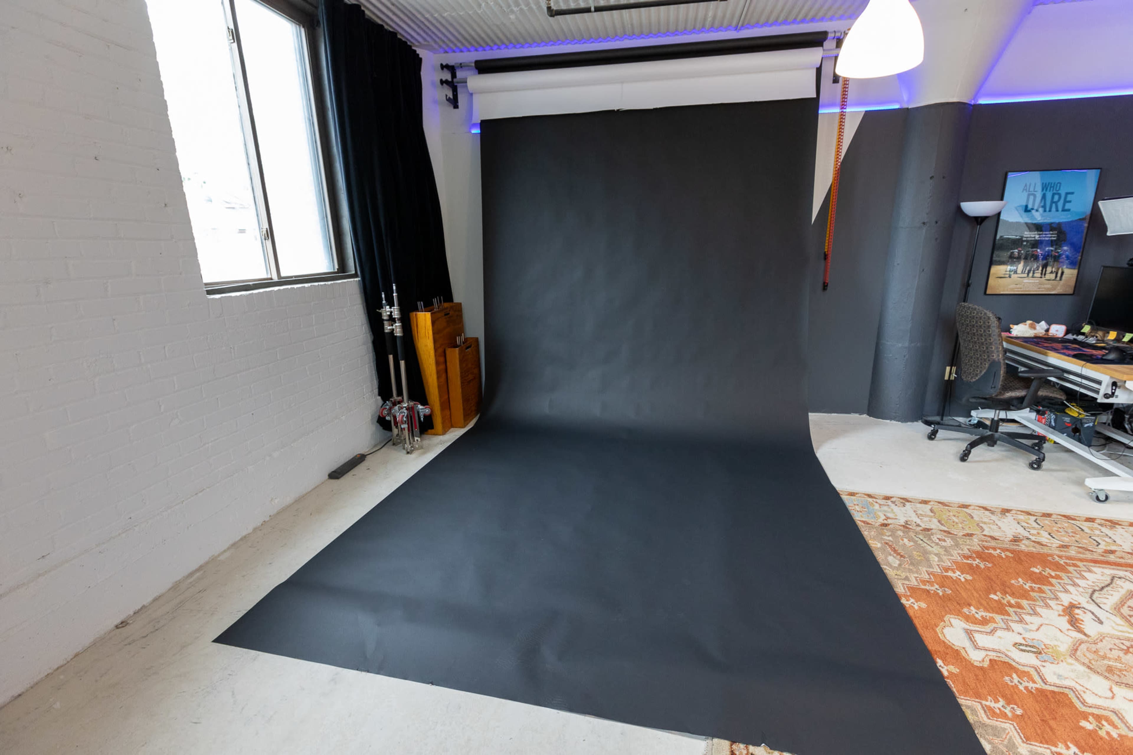 A photography studio with a black backdrop, a window, and a workspace featuring a chair and desk.