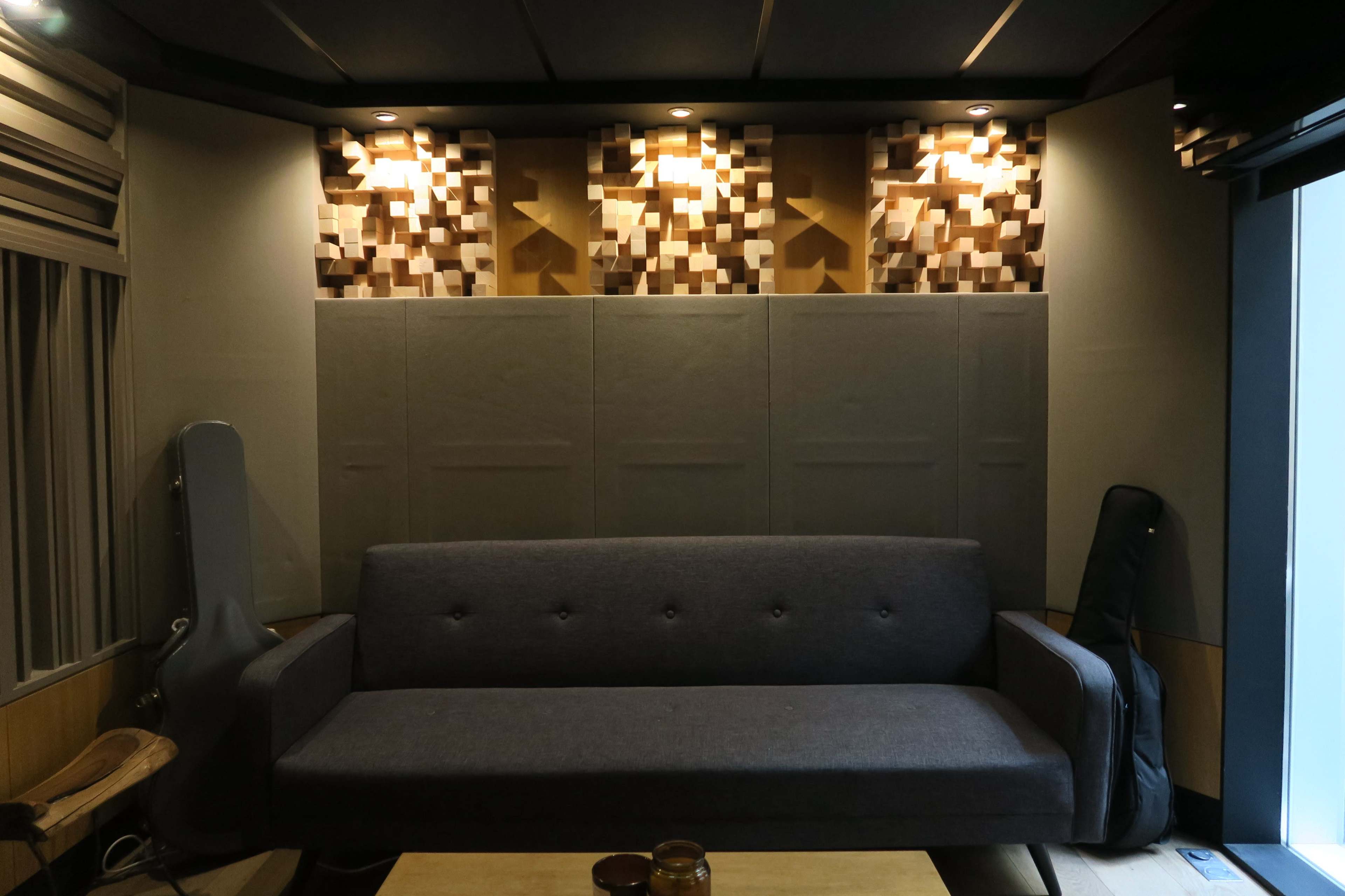 The image features a gray sofa positioned against a wall with unique wood paneling and built-in lighting.