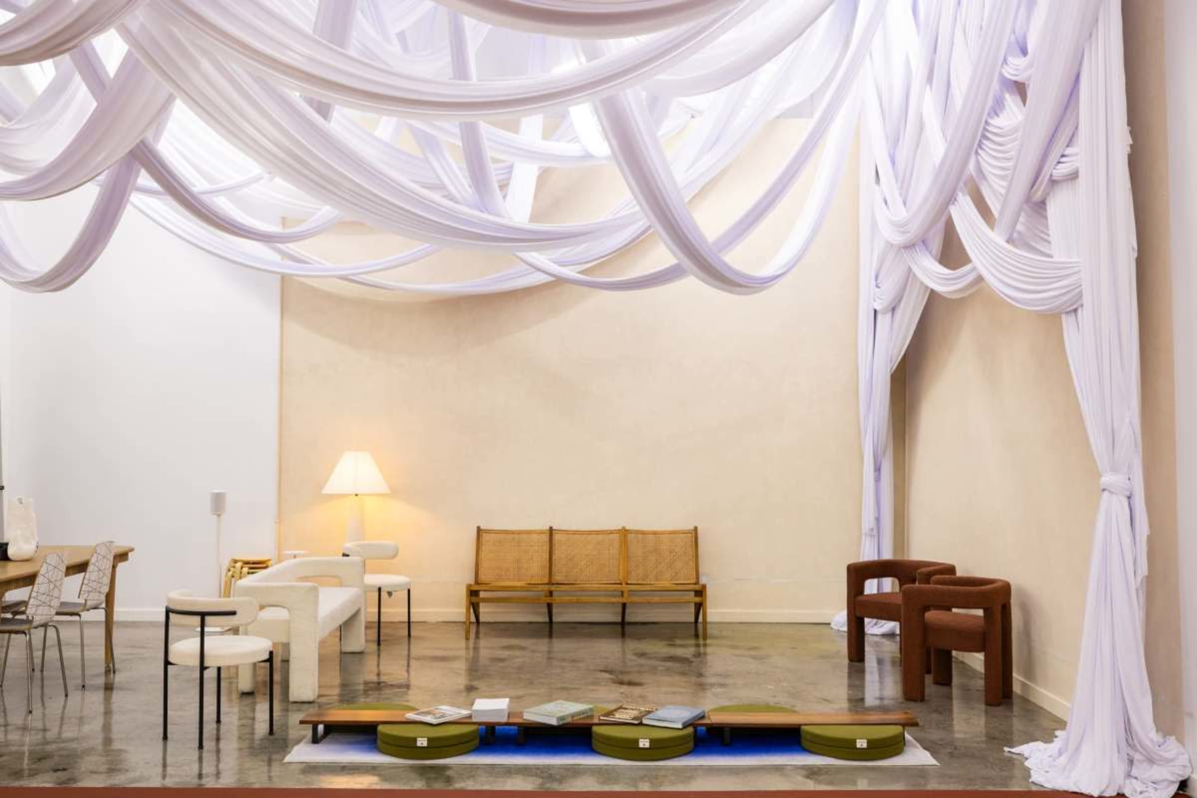 The image shows an interior space with elegant draped fabric overhead, featuring minimalist furniture arranged around a central low table.