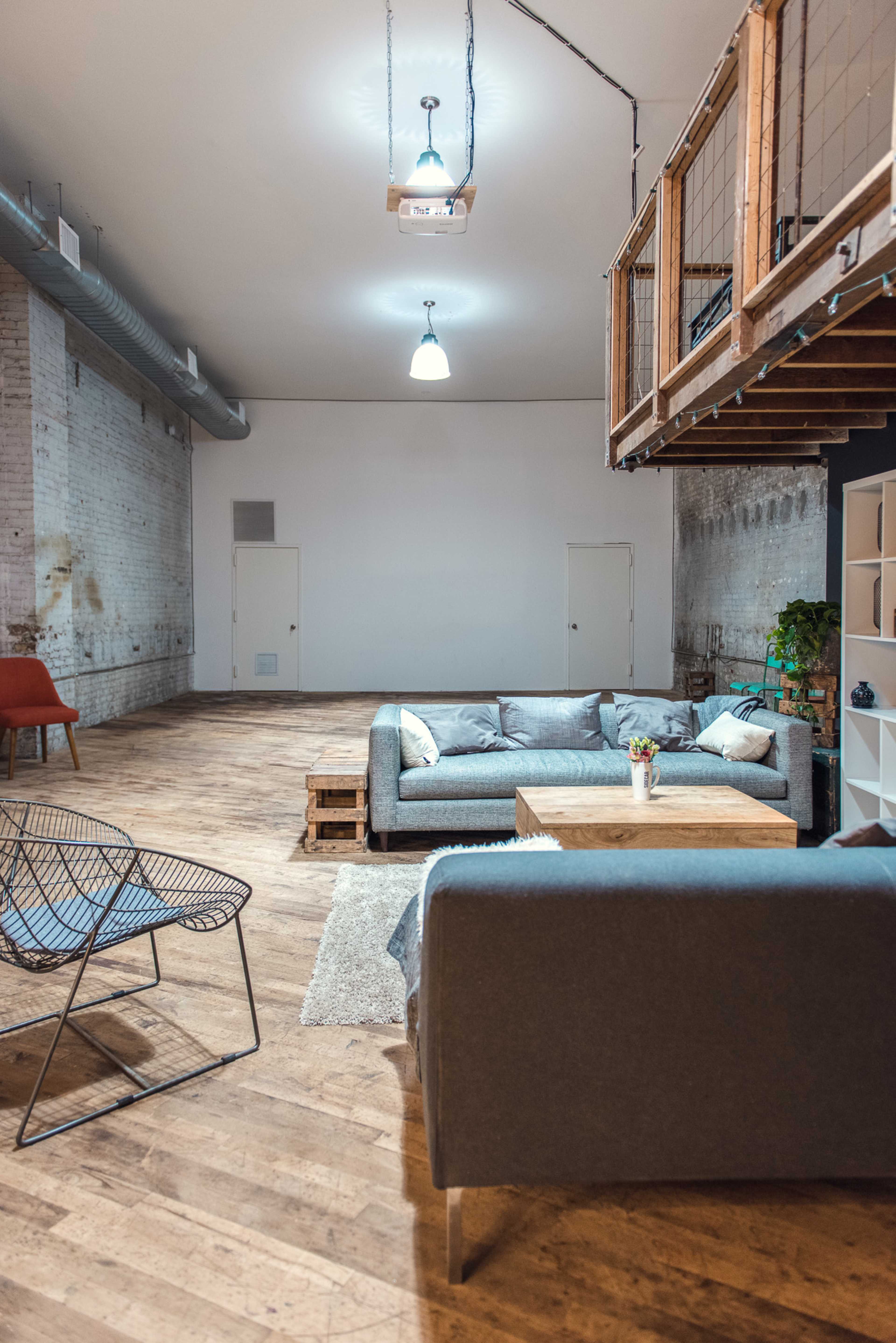 A spacious, minimalist interior featuring a gray sofa, a wooden coffee table, and a wire chair, with a lofted area in the background.