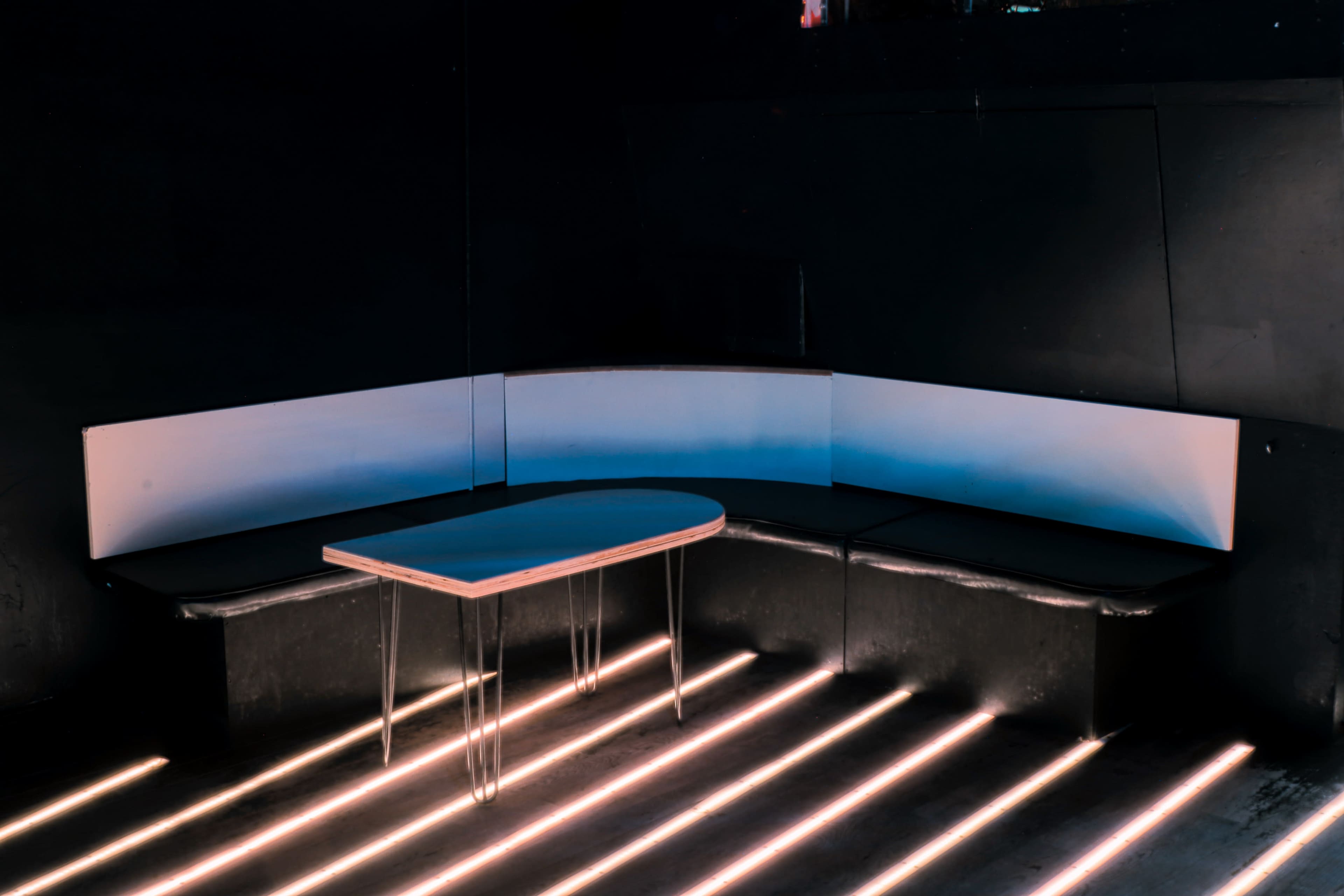 A dimly lit corner features a minimalist seating area with a table and angular bench.
