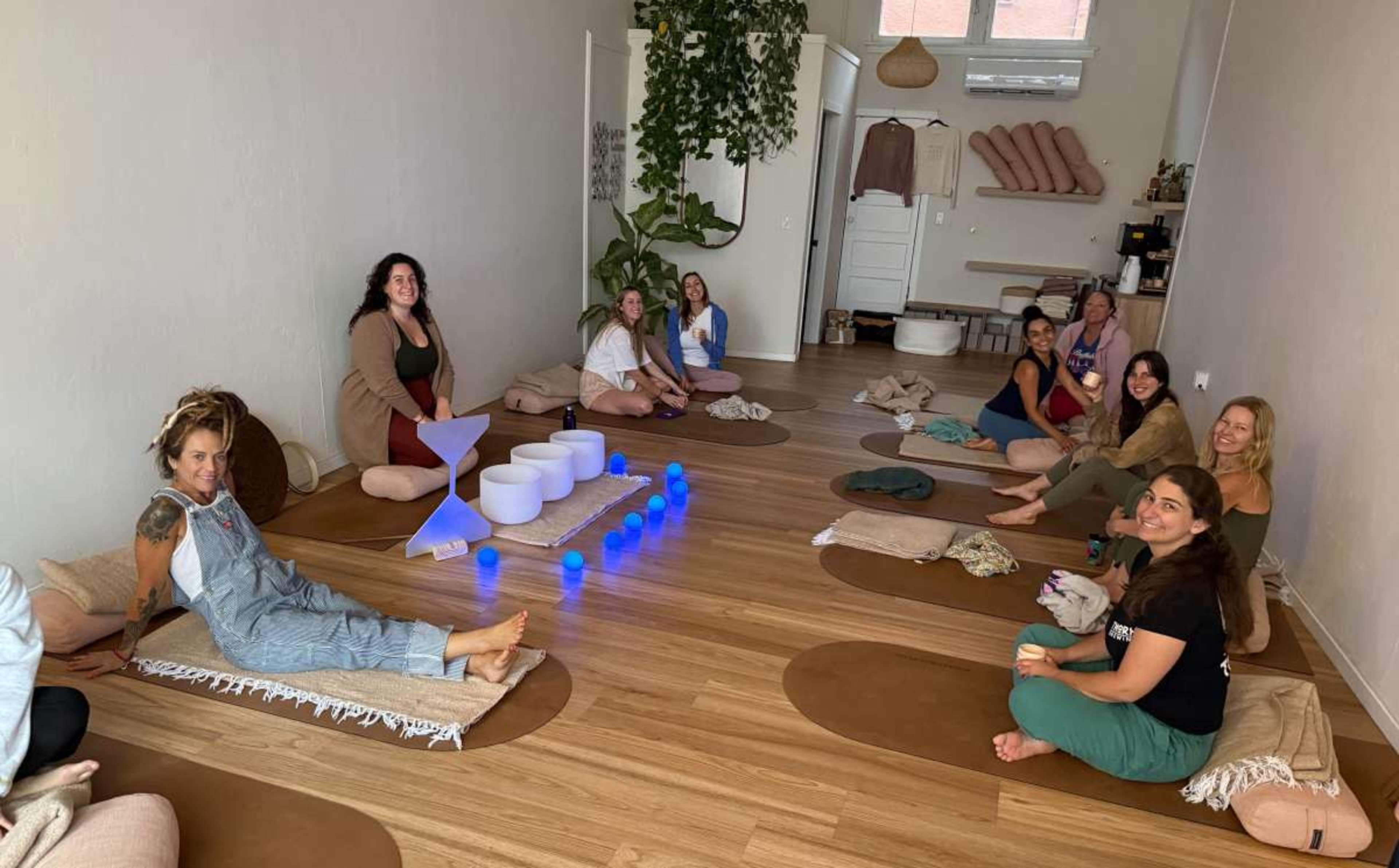 A group of people participates in a wellness session in a serene indoor space with mats and soft lighting.