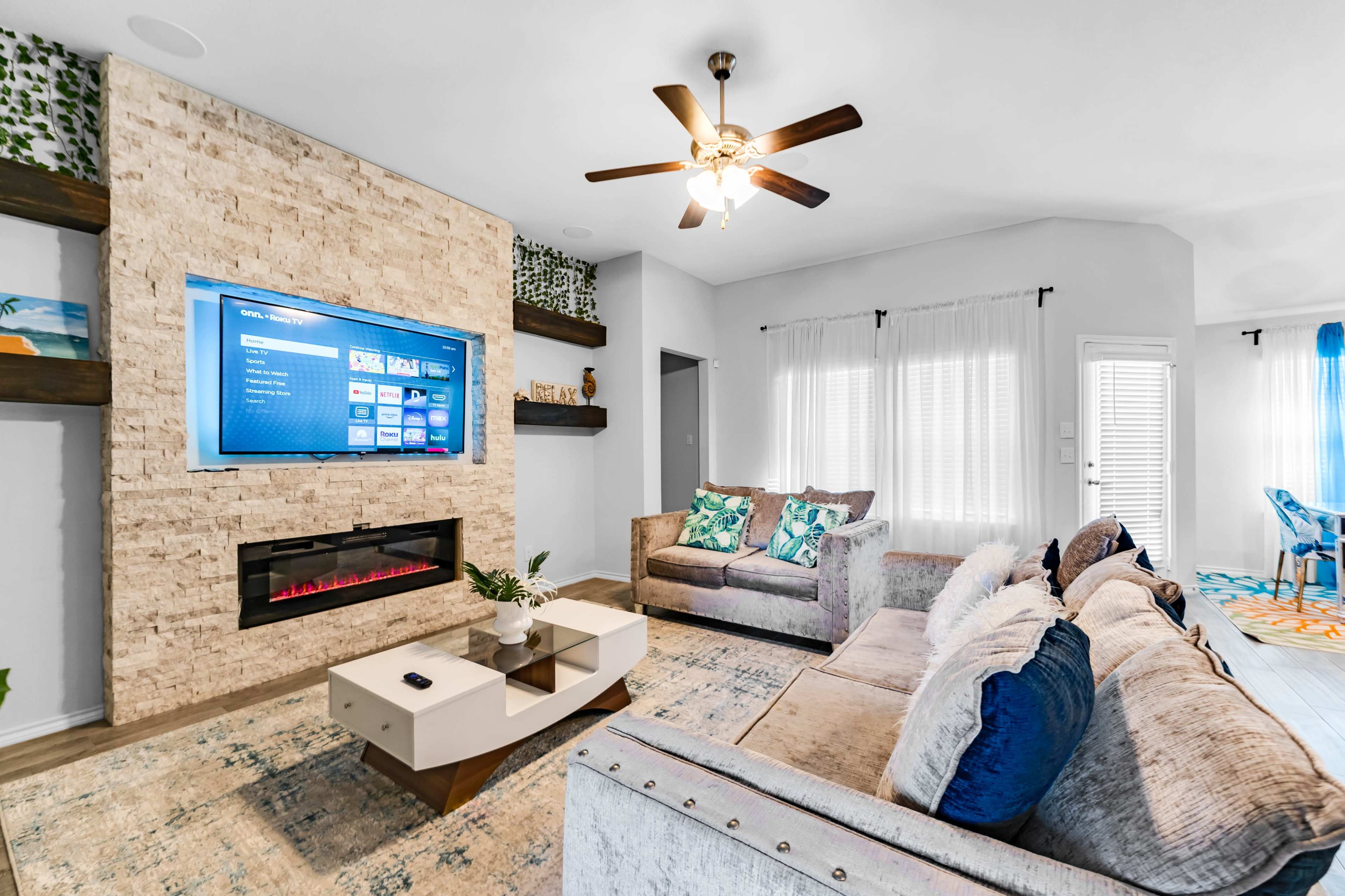 A modern living room with a television mounted on a stone wall, complemented by a decorative electric fireplace and contemporary furniture.