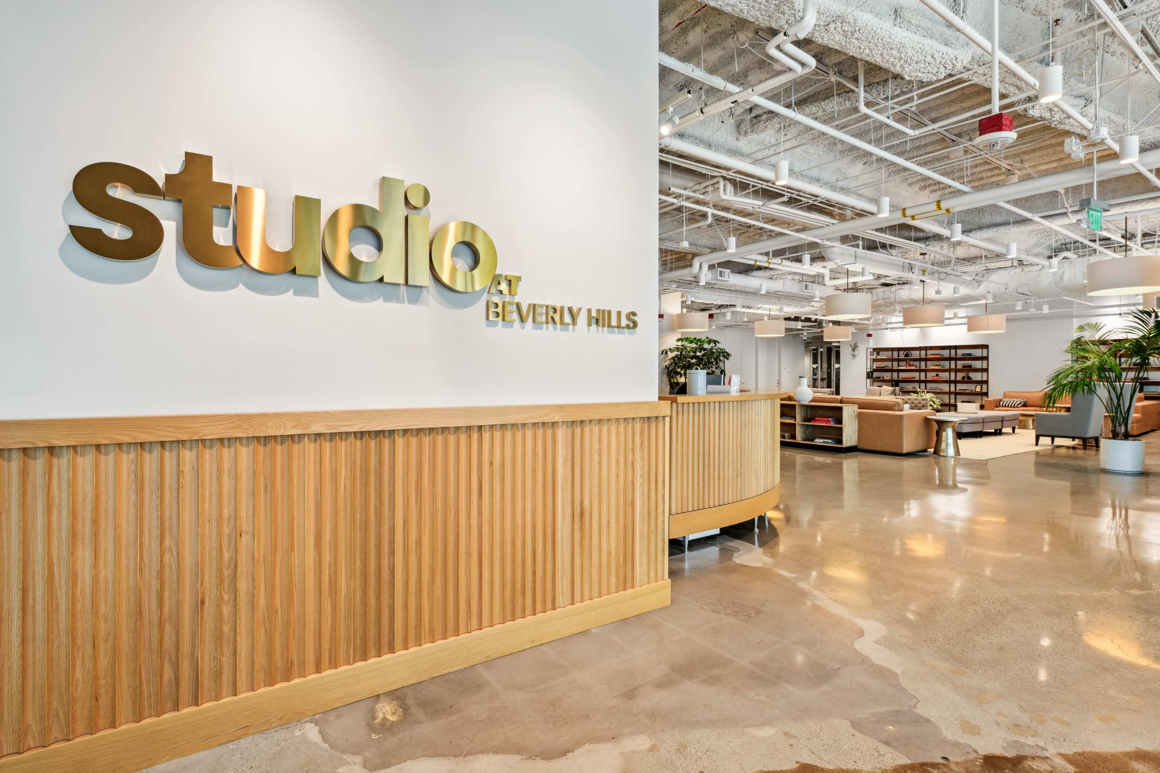 The image shows a modern office lobby with a reception area featuring a wooden counter and a sign that reads "studio at BEVERLY HILLS."