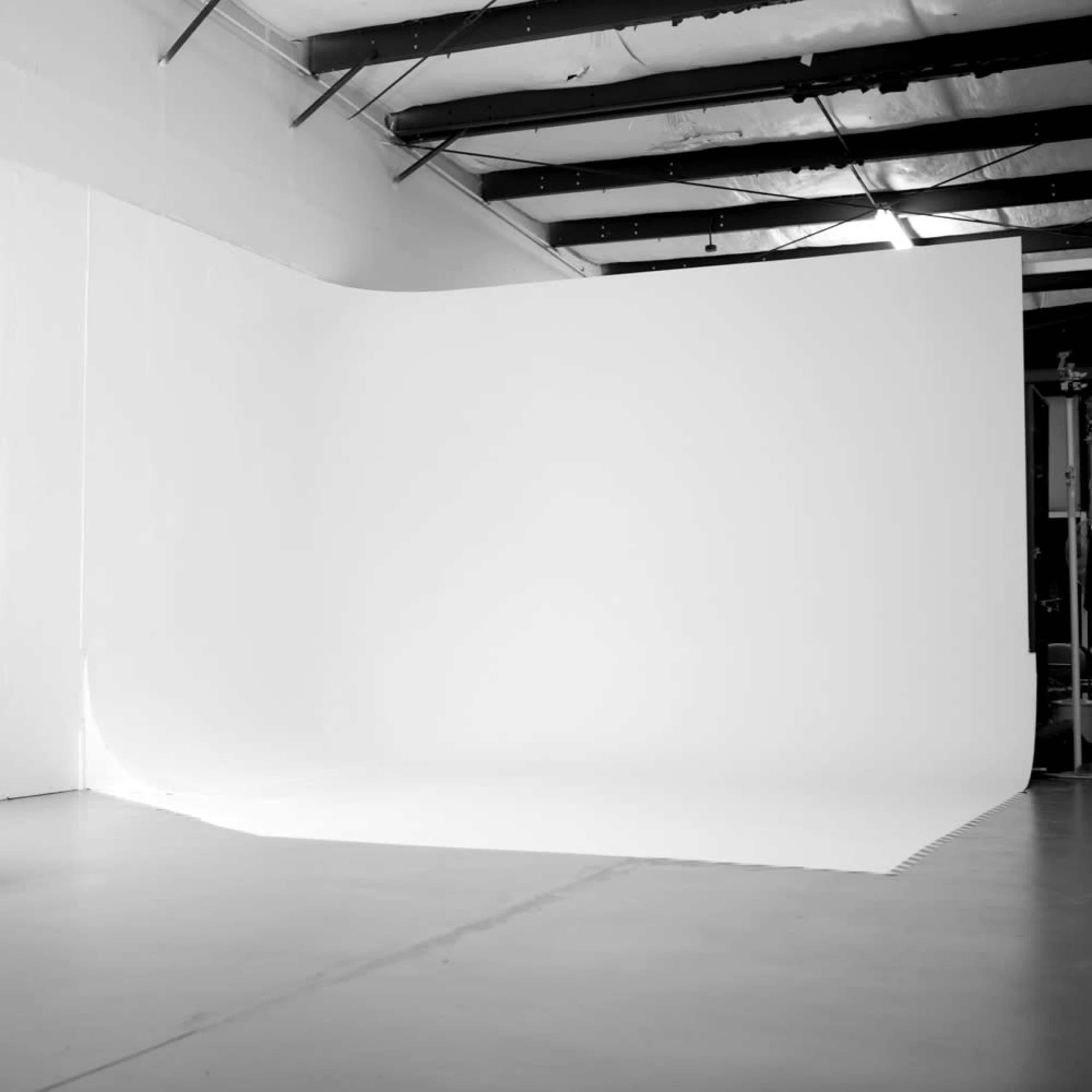 A spacious, empty studio with a large white backdrop and a smooth floor.
