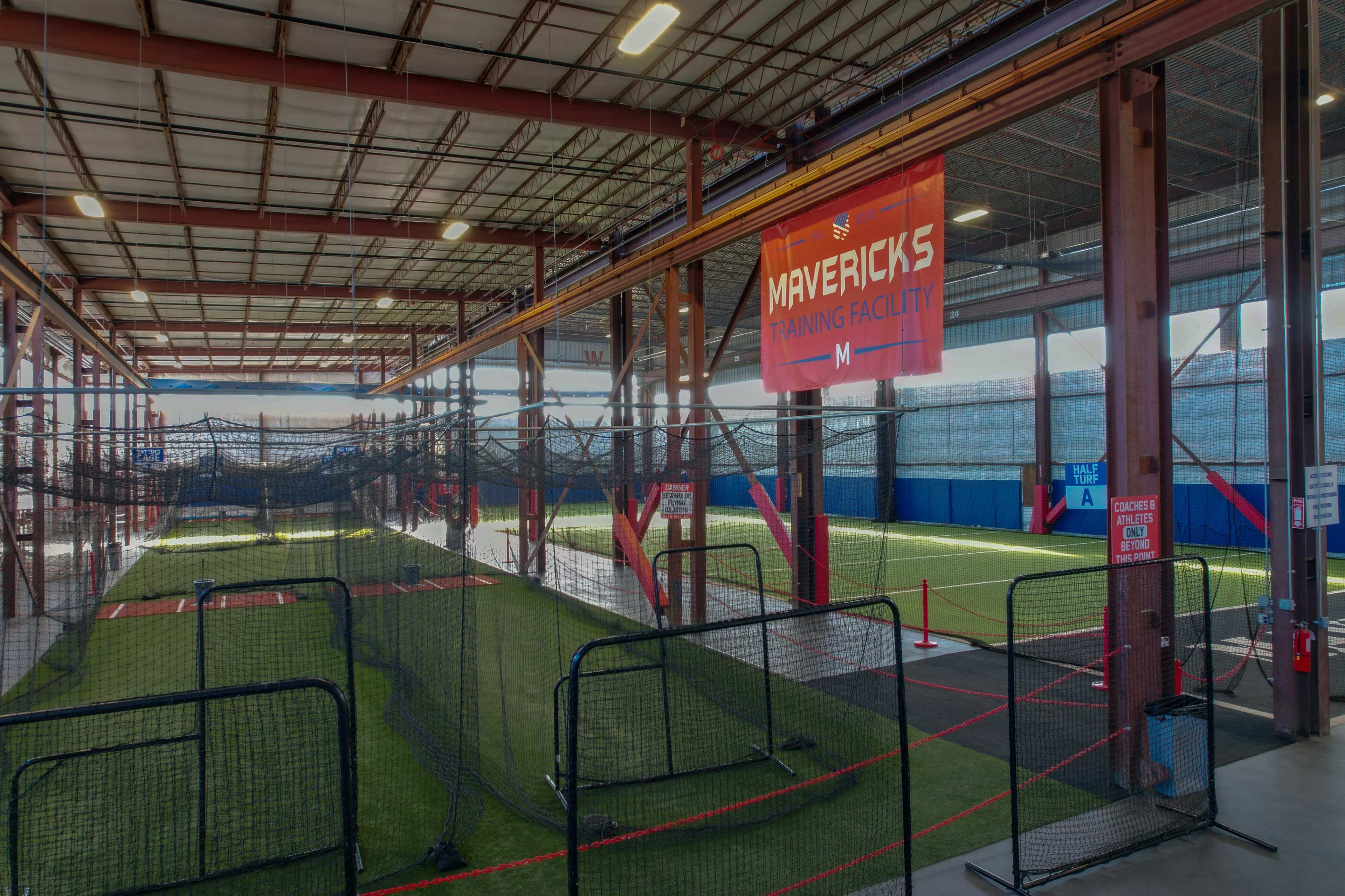 The interior of the Mavericks Training Facility, featuring a turf area surrounded by netting and training equipment.