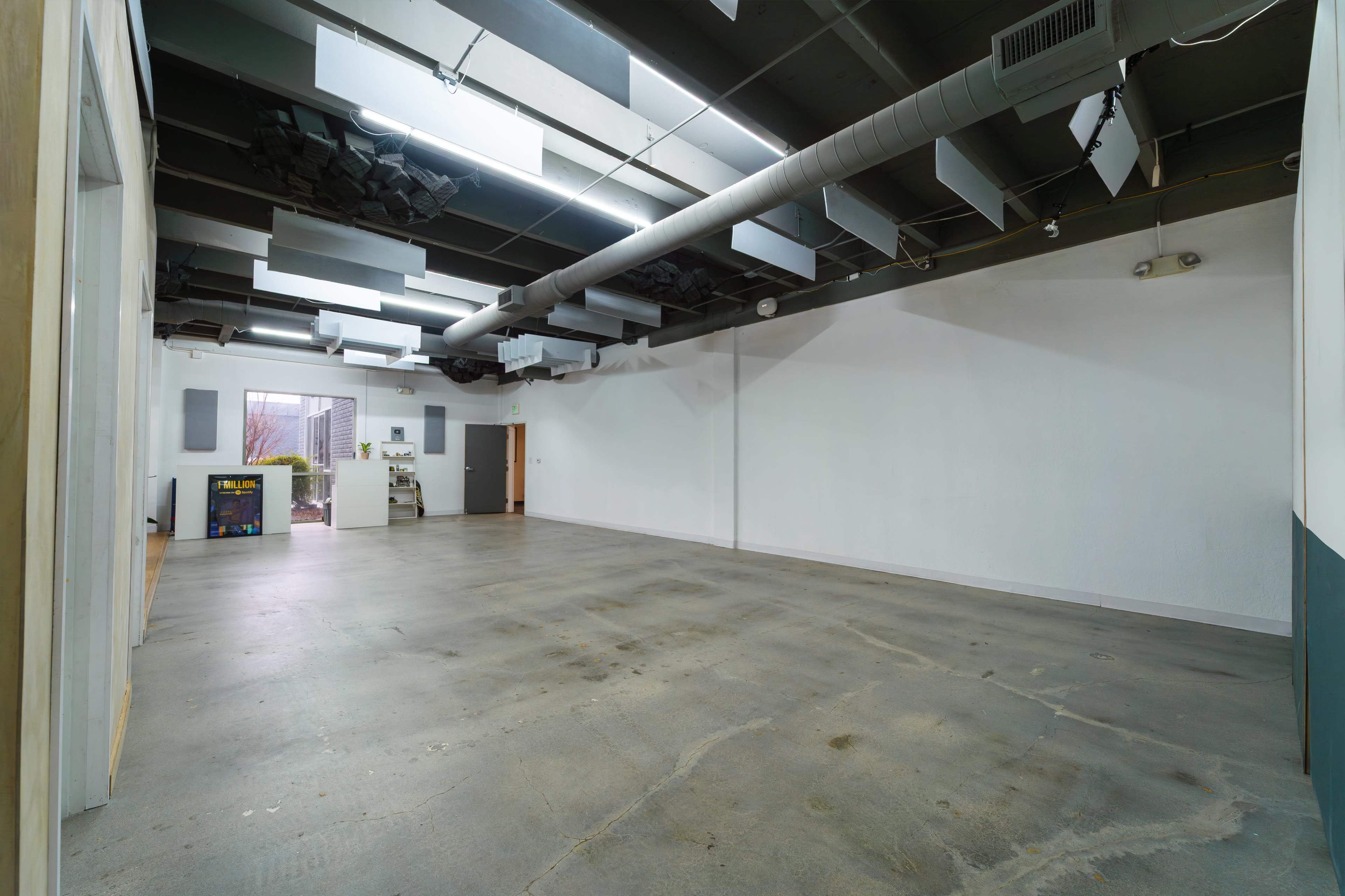 The image shows an empty indoor space with concrete flooring and a set of large acoustic panels on the ceiling.