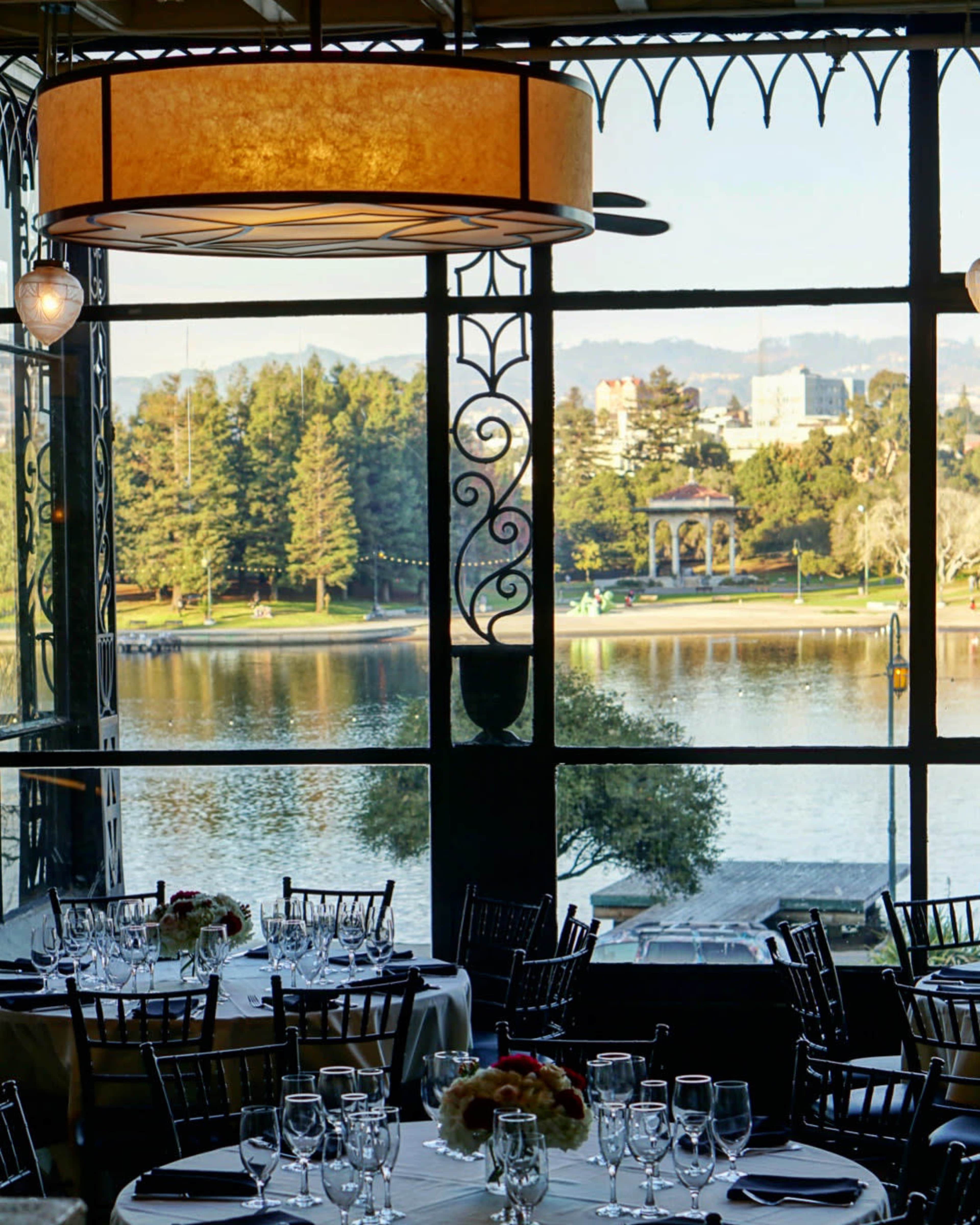 The image shows a well-decorated restaurant interior with tables set for dining and a view of a lake and trees through large windows.