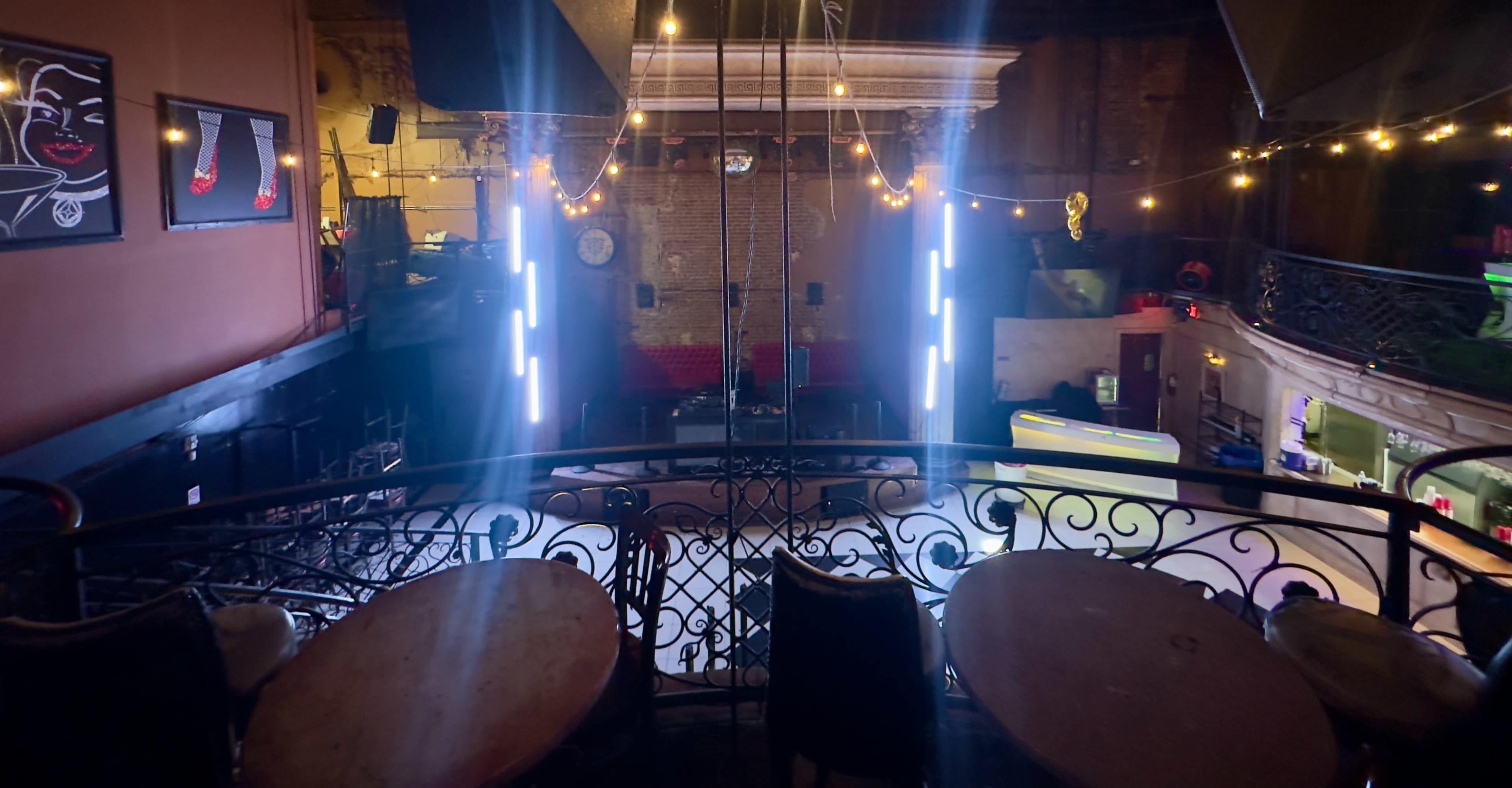 The image shows a dimly lit venue with a stage illuminated by vertical lights and several seating areas visible from a balcony.