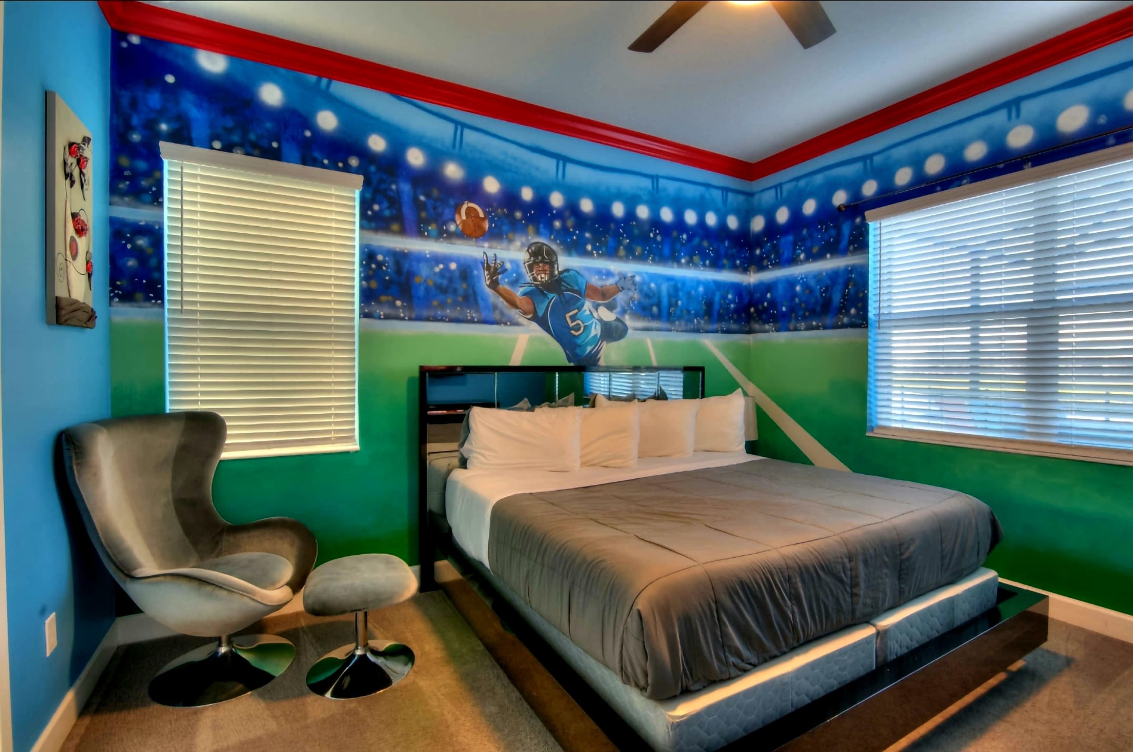 A bedroom features a large mural of a football player on the wall, with a bed, modern chair, and window with blinds.