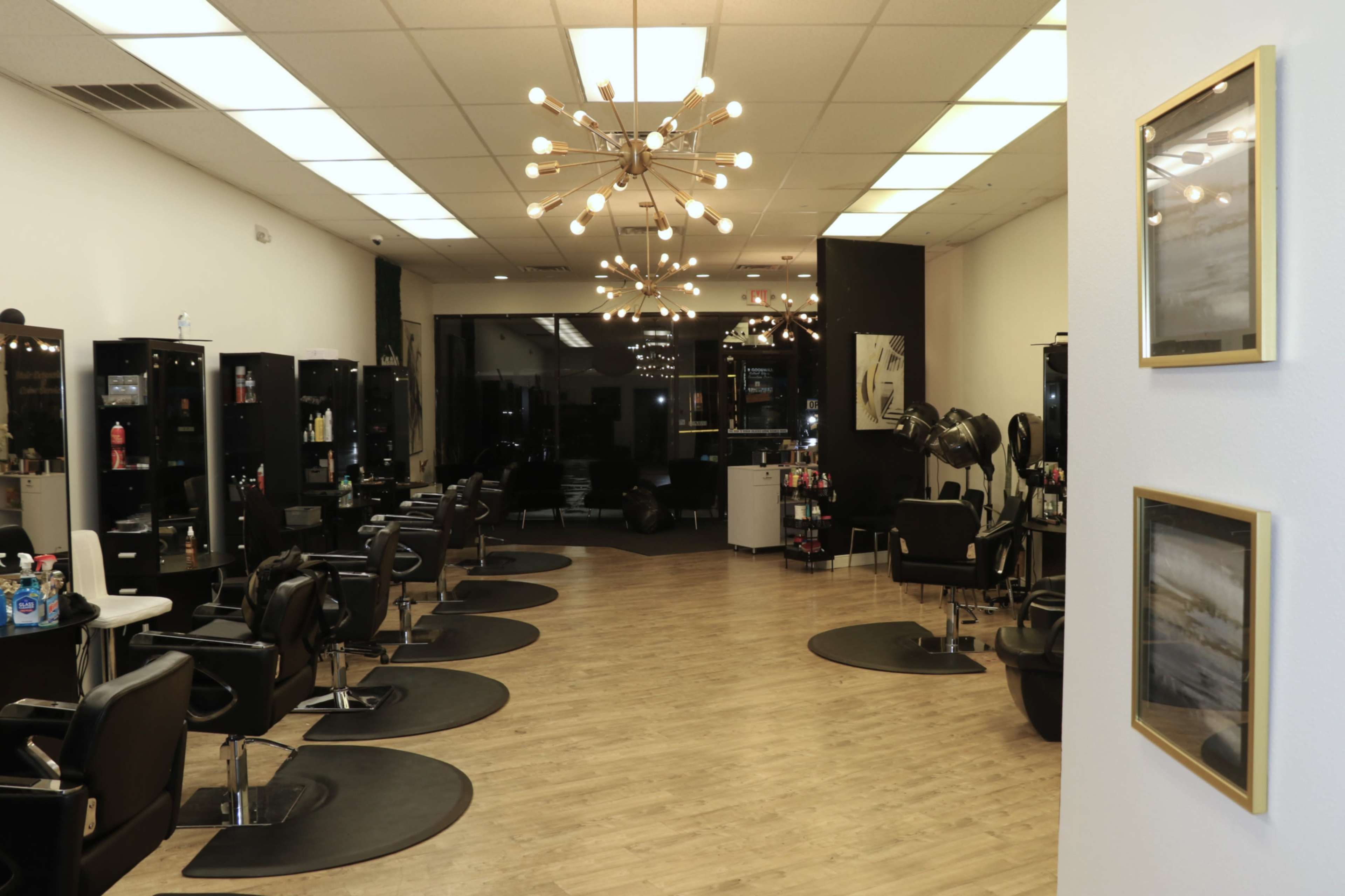 The image shows a modern hair salon with multiple styling stations, black chairs, and decorative lighting.