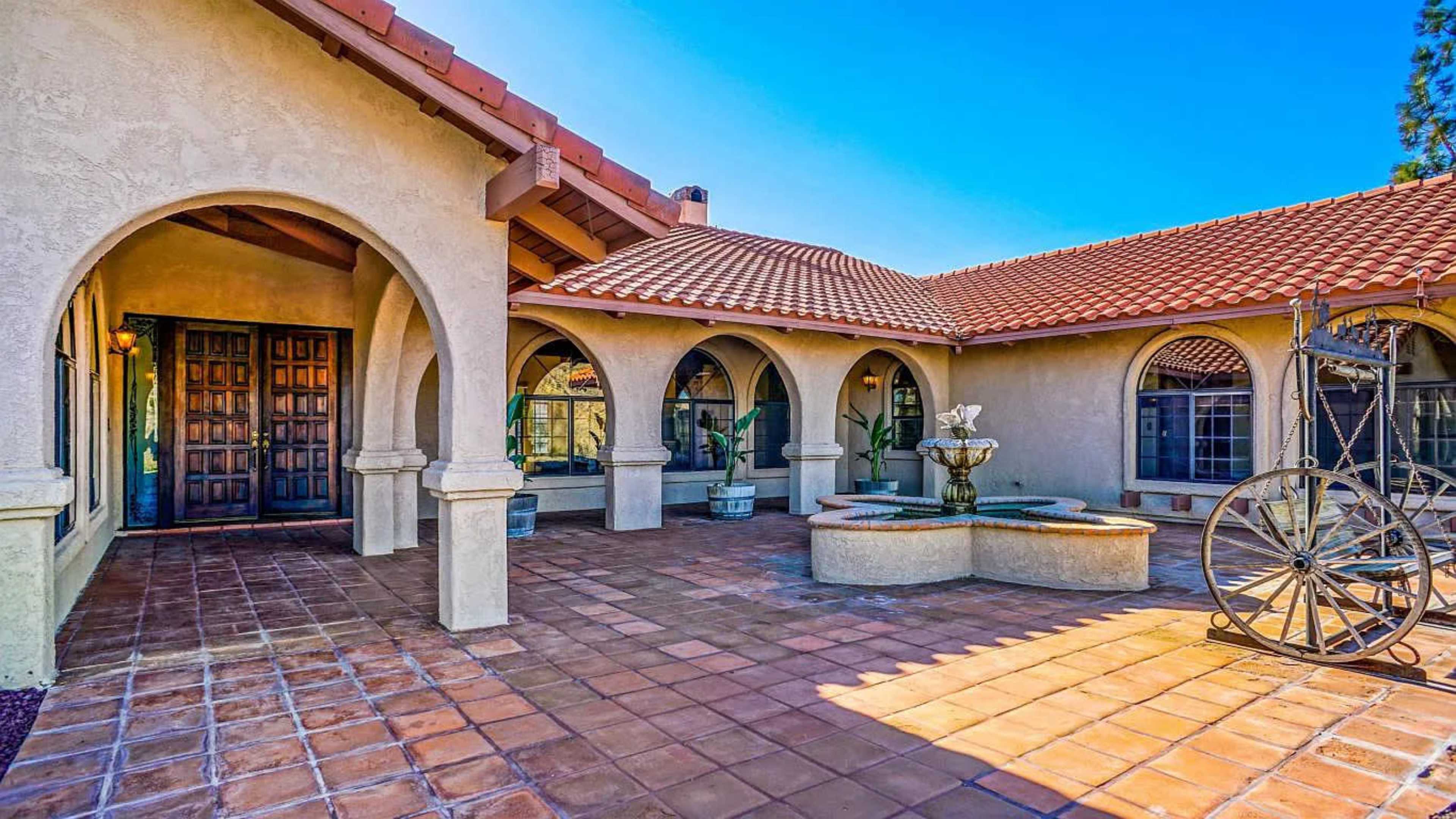 A courtyard entrance of a house featuring arched doorways, a fountain, and a tile-paved surface.
