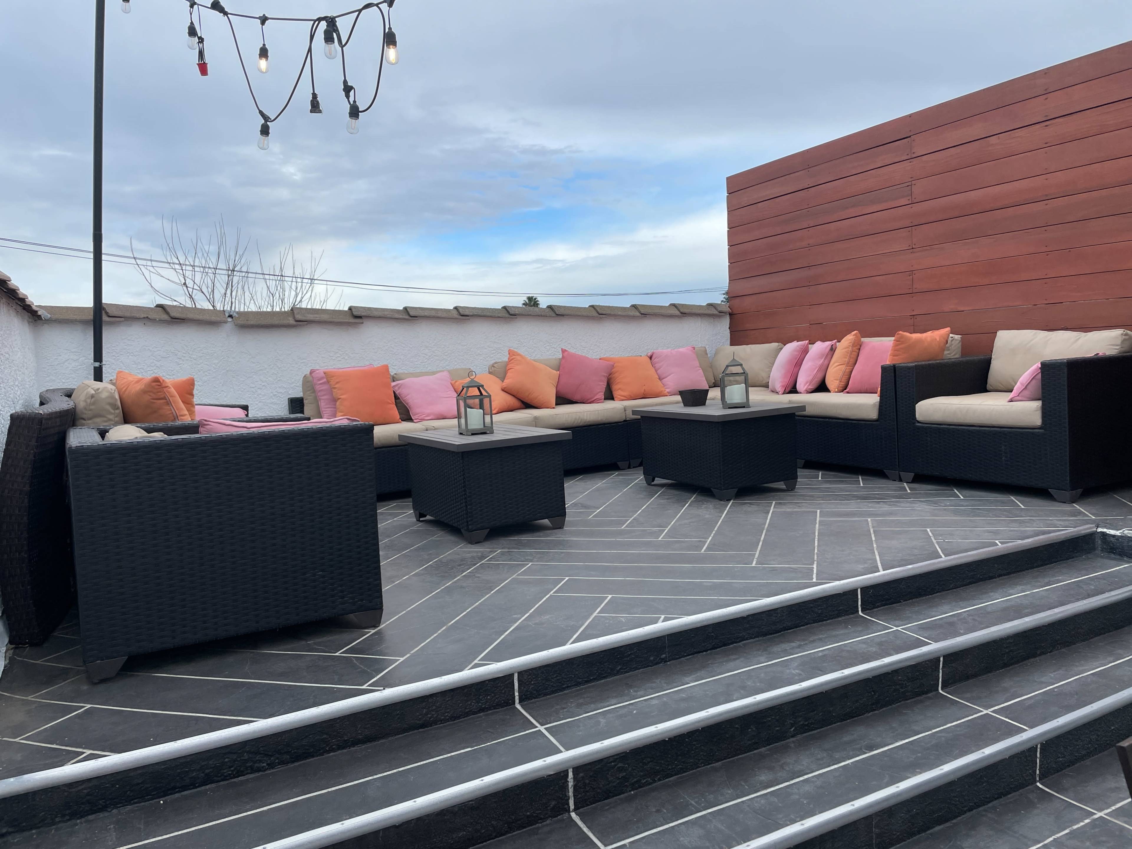 A stylish outdoor seating area with black wicker furniture, pink and beige cushions, and a modern stone tile floor.