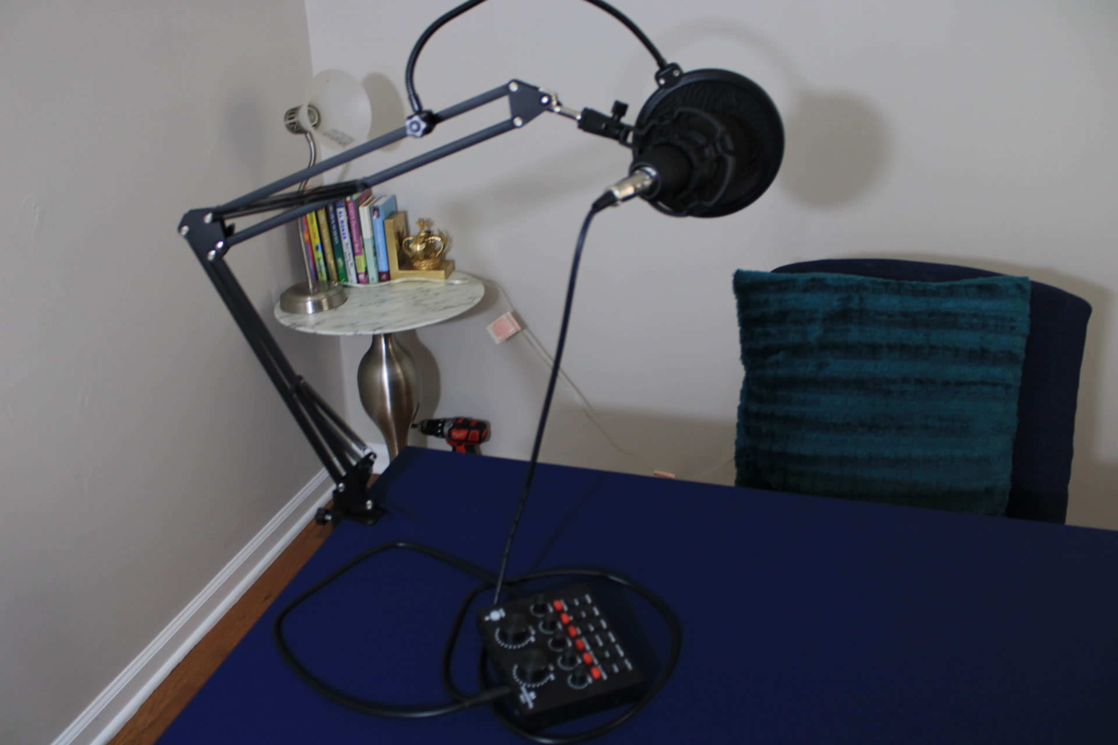 A microphone mounted on an adjustable arm is positioned on a blue tablecloth next to a modern-style side table with books and a decorative item.