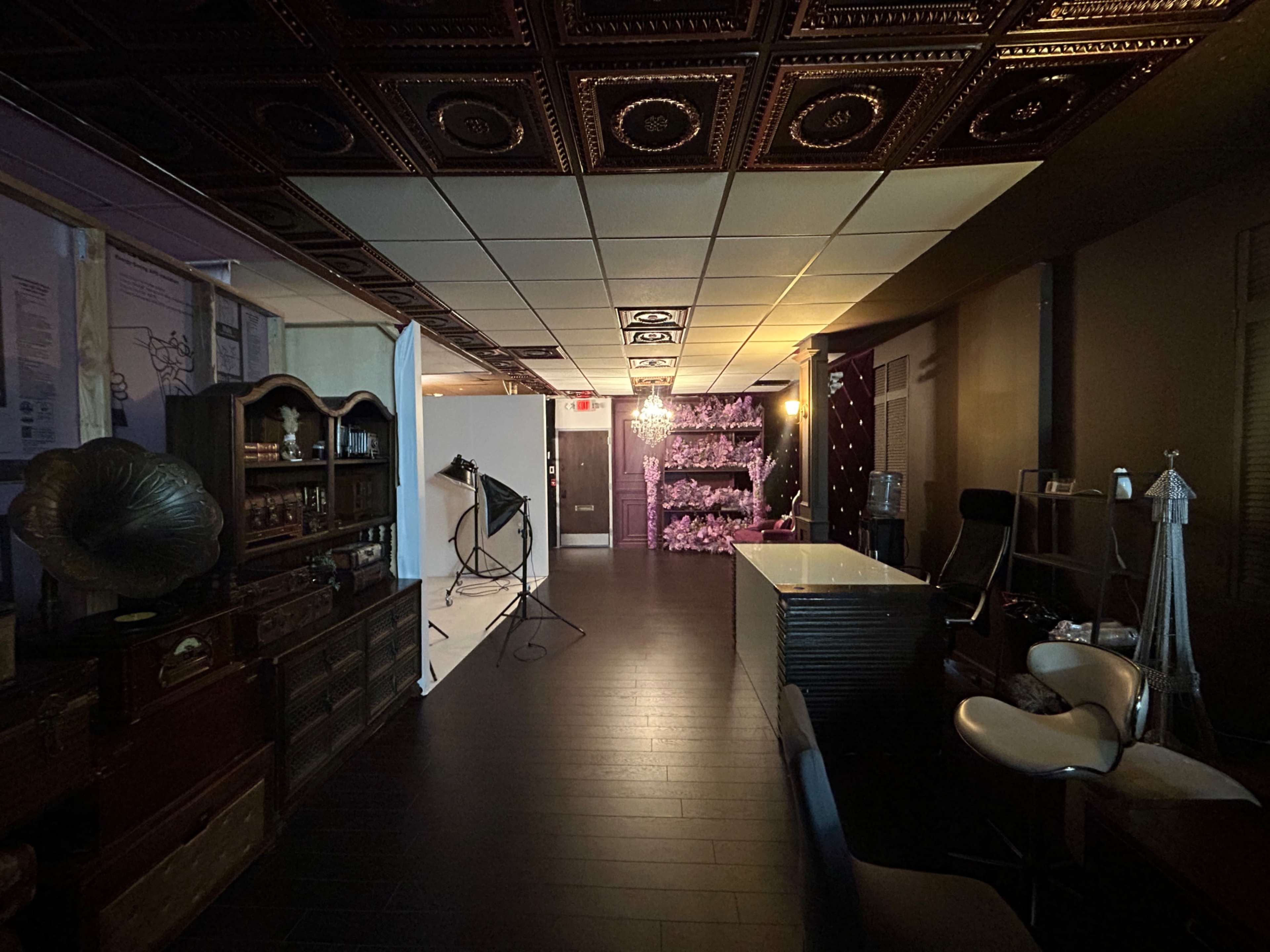 The image shows a spacious interior with dark flooring, a prominent reception desk, and a mix of decorative elements, including a vintage phonograph and a backdrop with string lights.