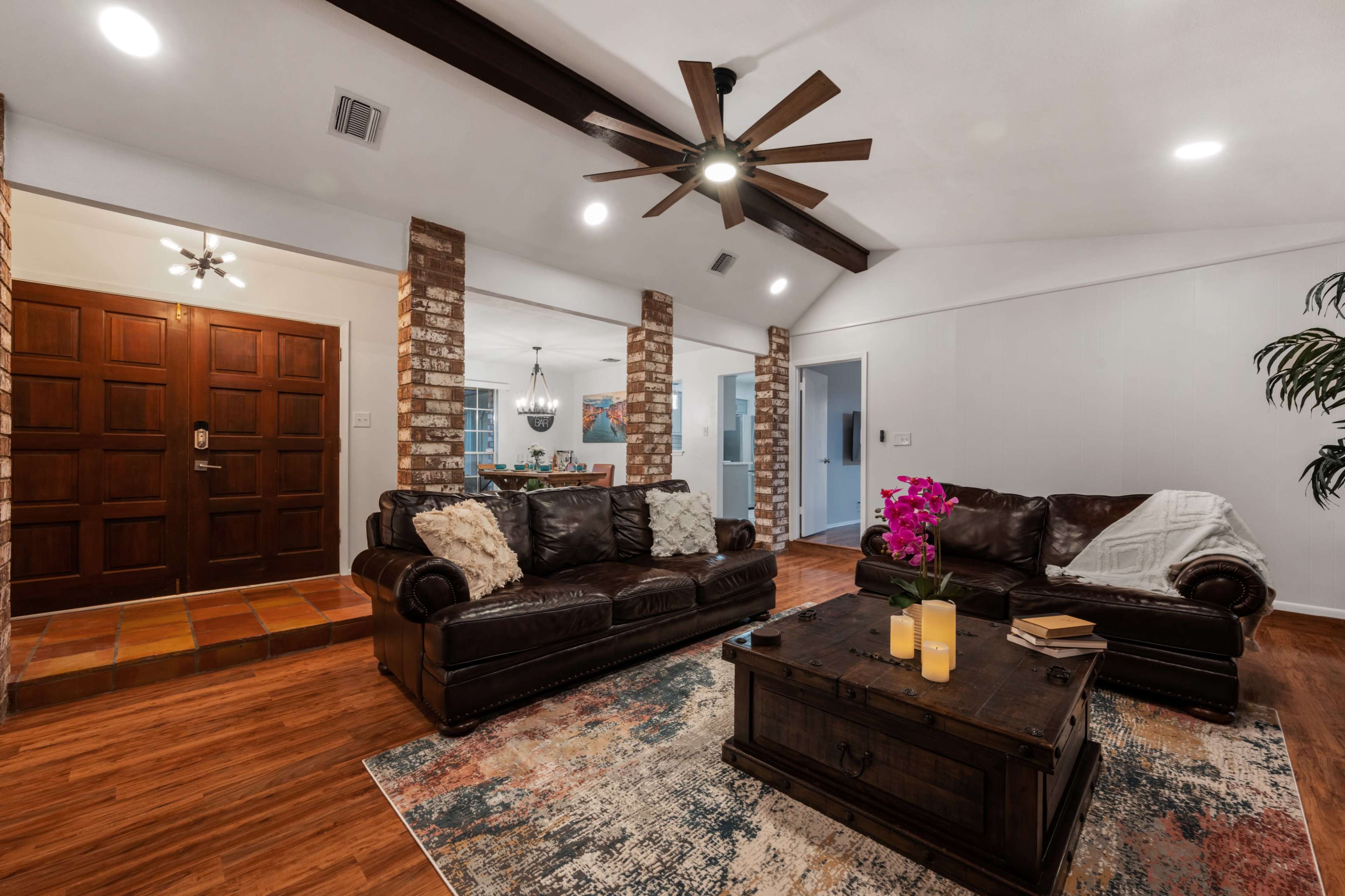 The living room features dark leather sofas, a wooden coffee table with candles, and a brick accent wall near the entrance.