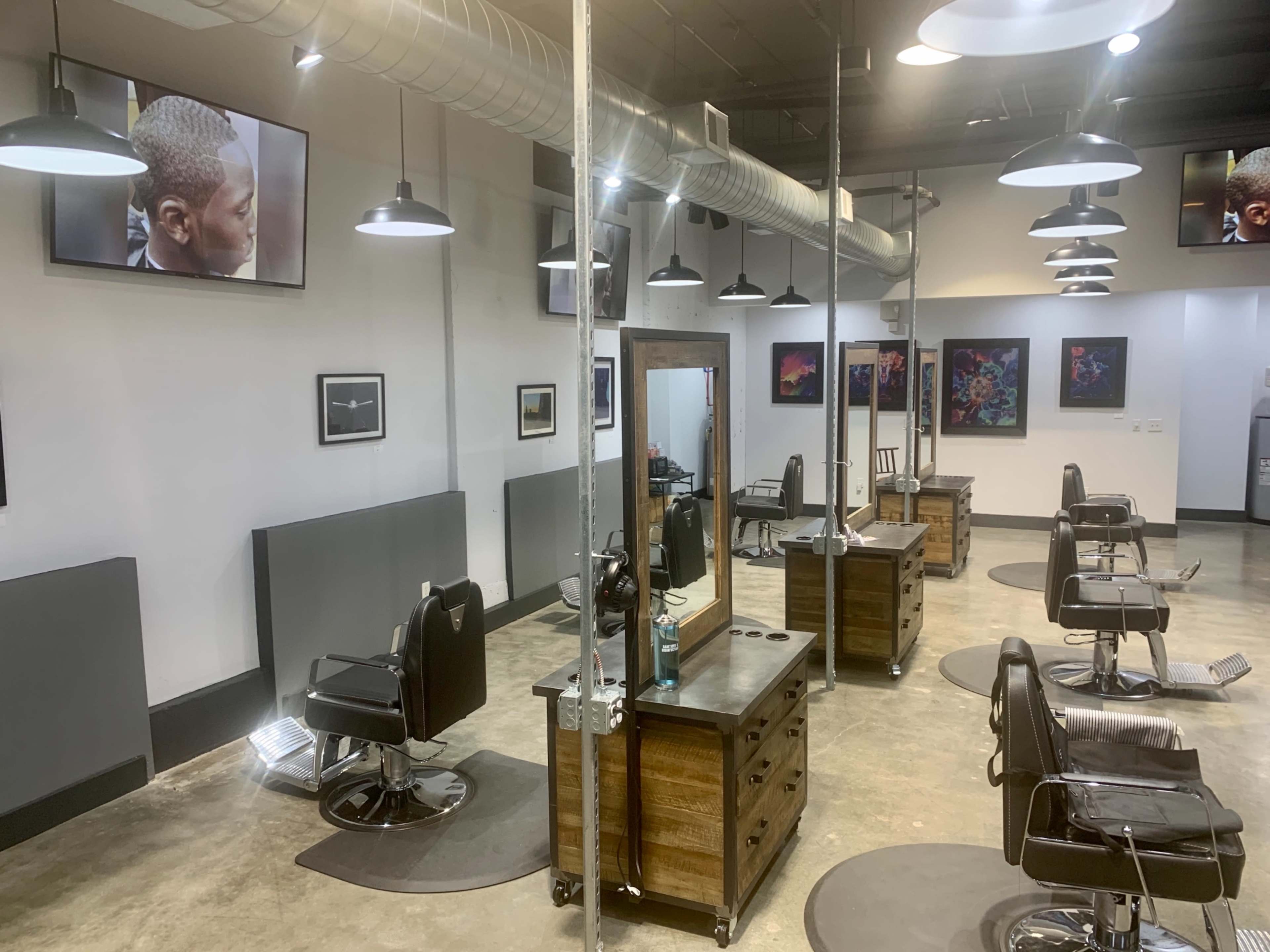 A modern hair salon features several styling stations with black chairs, large mirrors, and wall-mounted televisions displaying images.