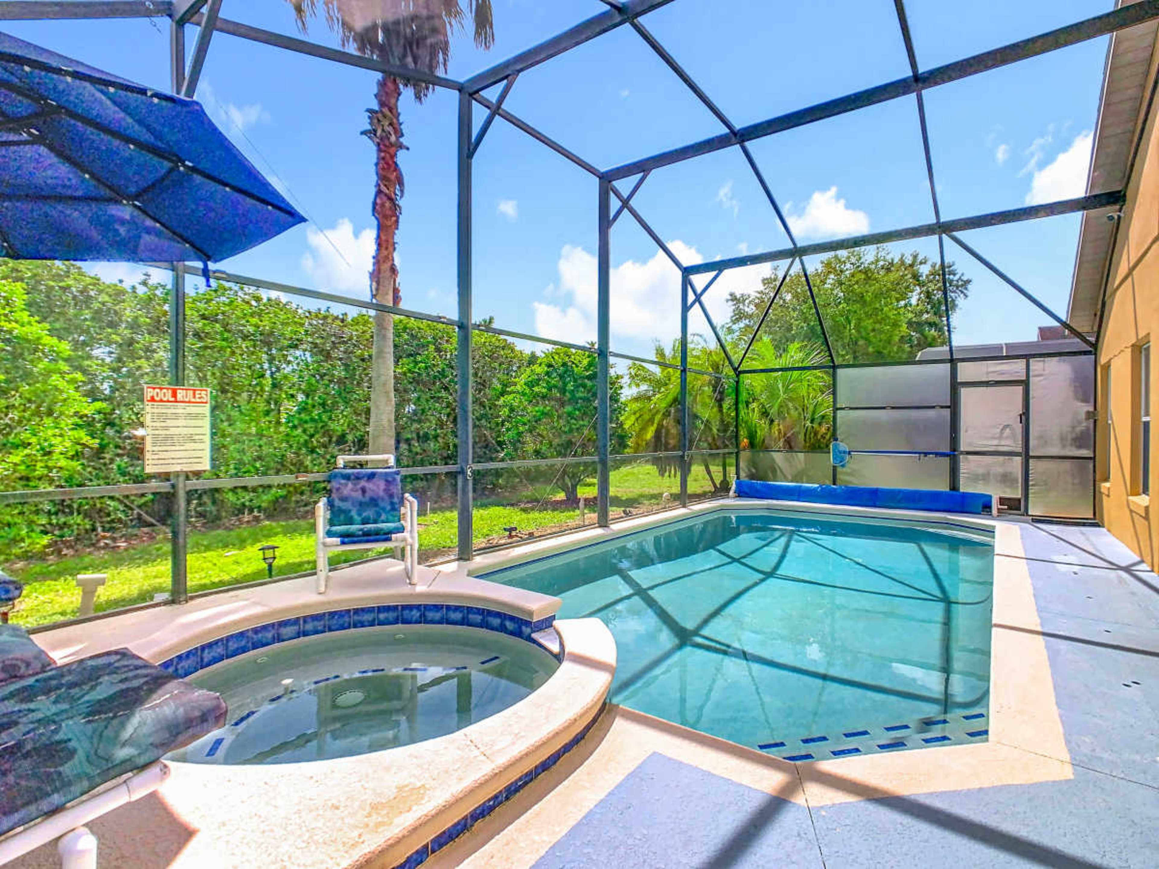 The image shows a screened-in swimming pool area with a small hot tub and lounge chairs, surrounded by greenery and palm trees.