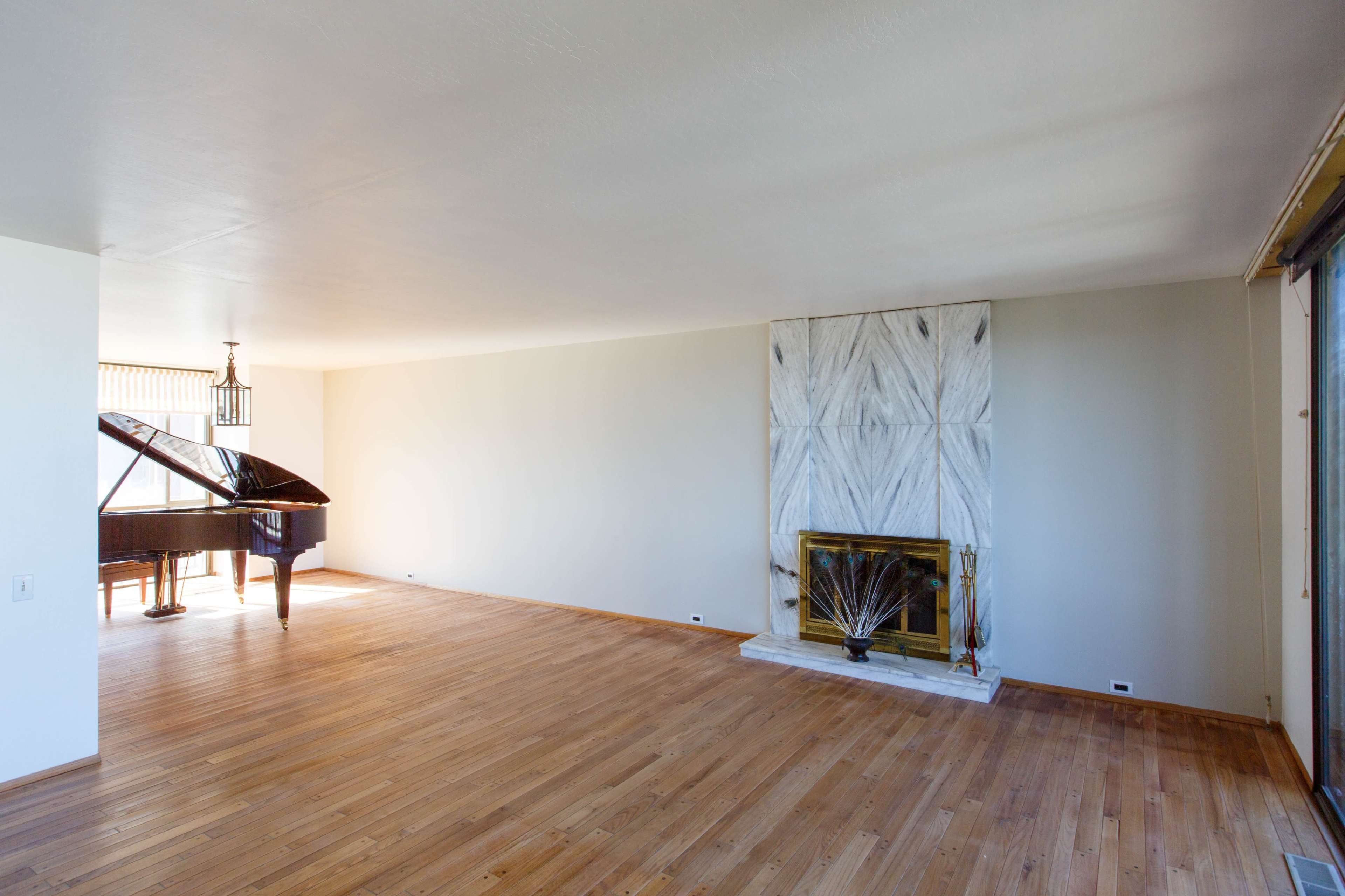 A spacious, empty room with a grand piano in one corner and a marble fireplace on one wall.