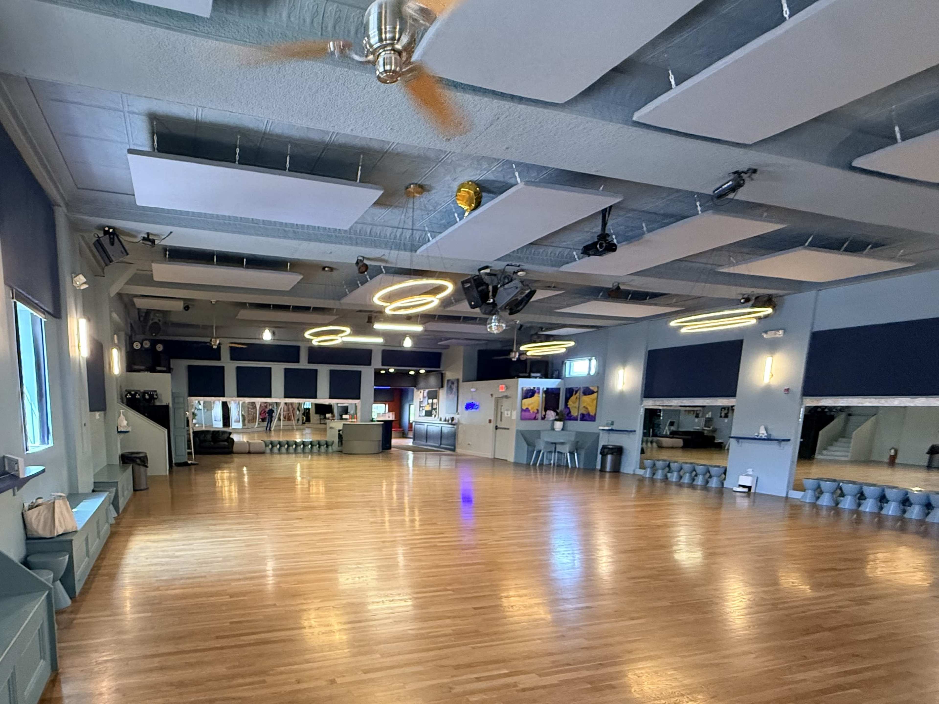 The image shows a spacious dance studio with wooden floors, high ceilings, and various lighting fixtures.