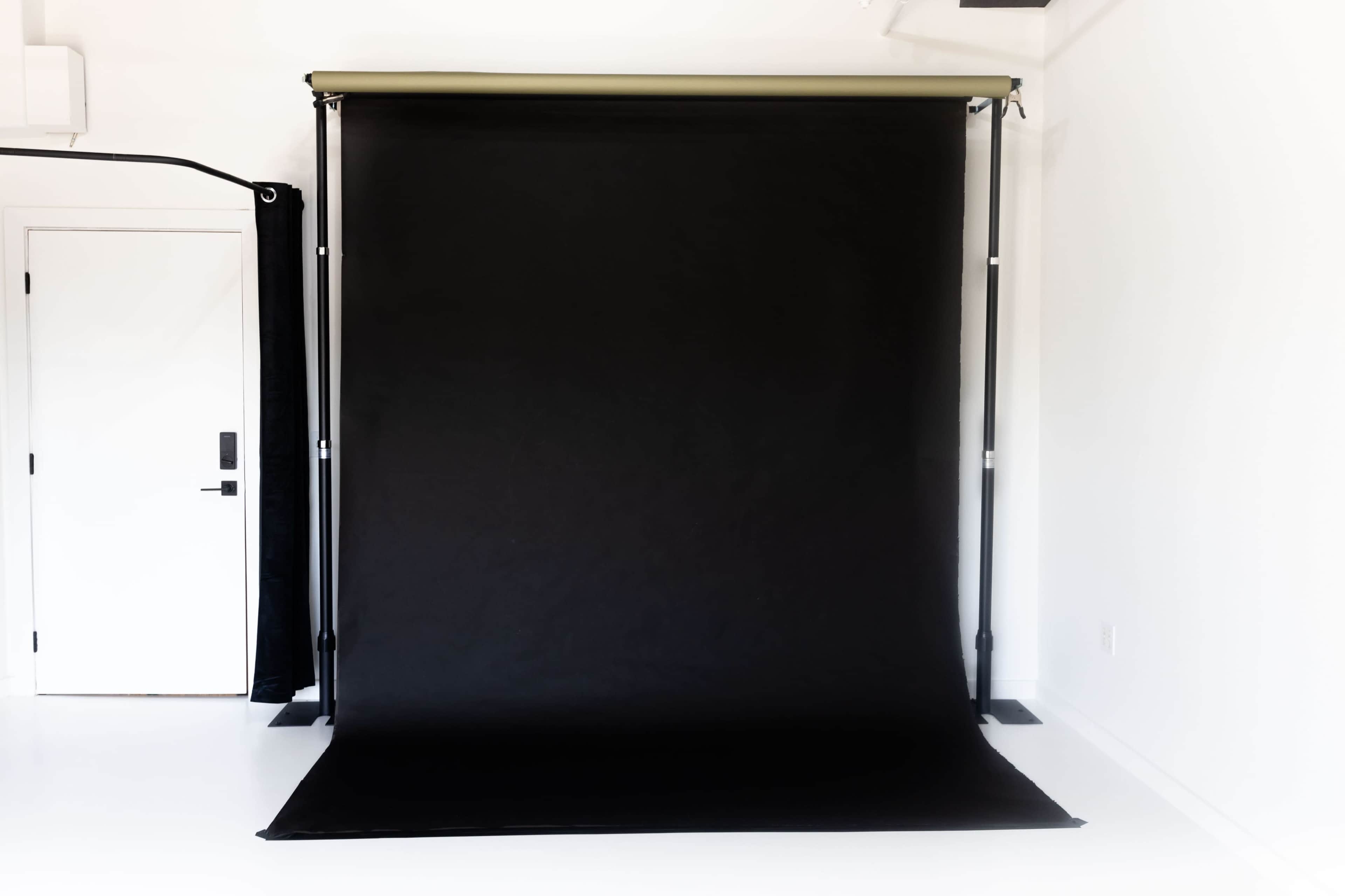 The image shows a black photography backdrop set up against a white wall in a studio space.