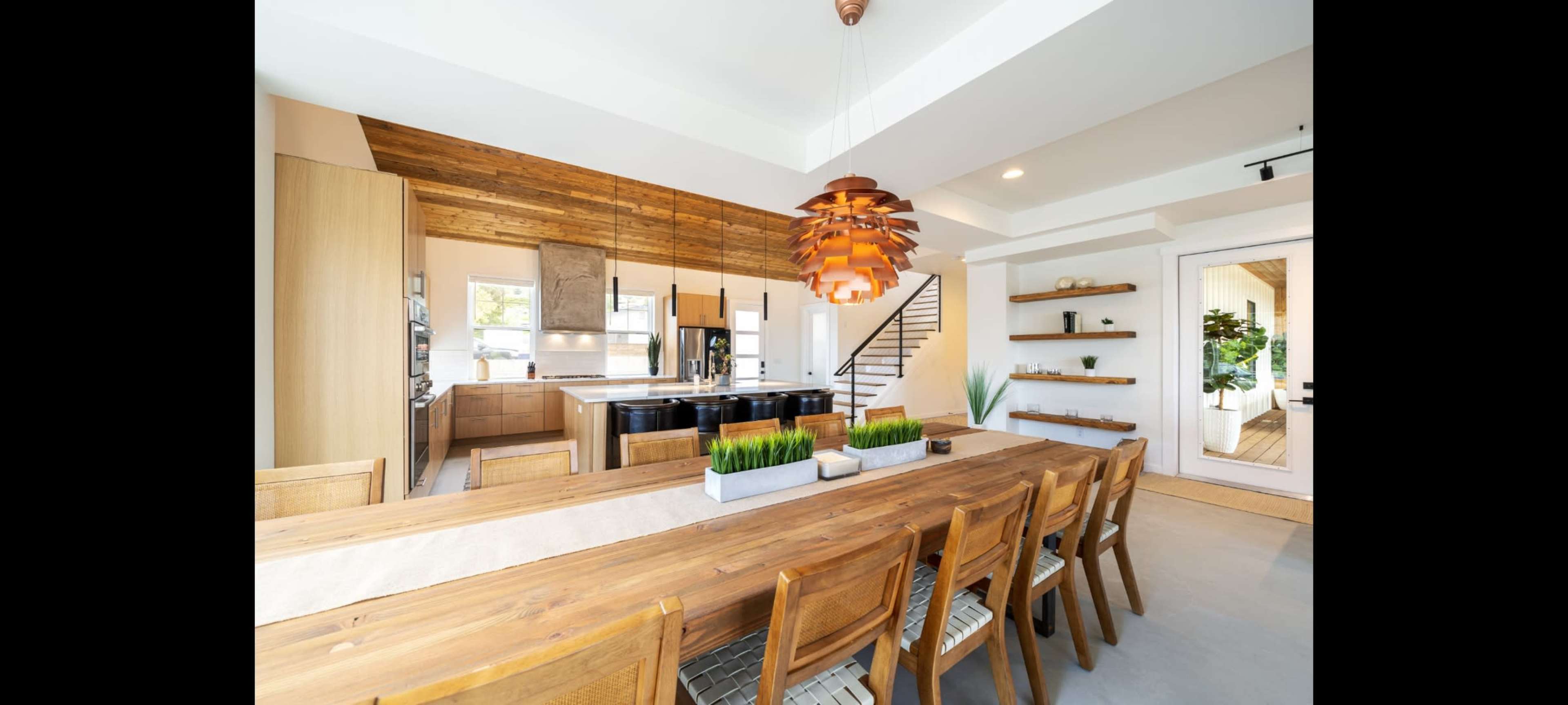 A spacious kitchen and dining area feature a large wooden table, modern lighting, and a mix of wooden and sleek cabinetry.