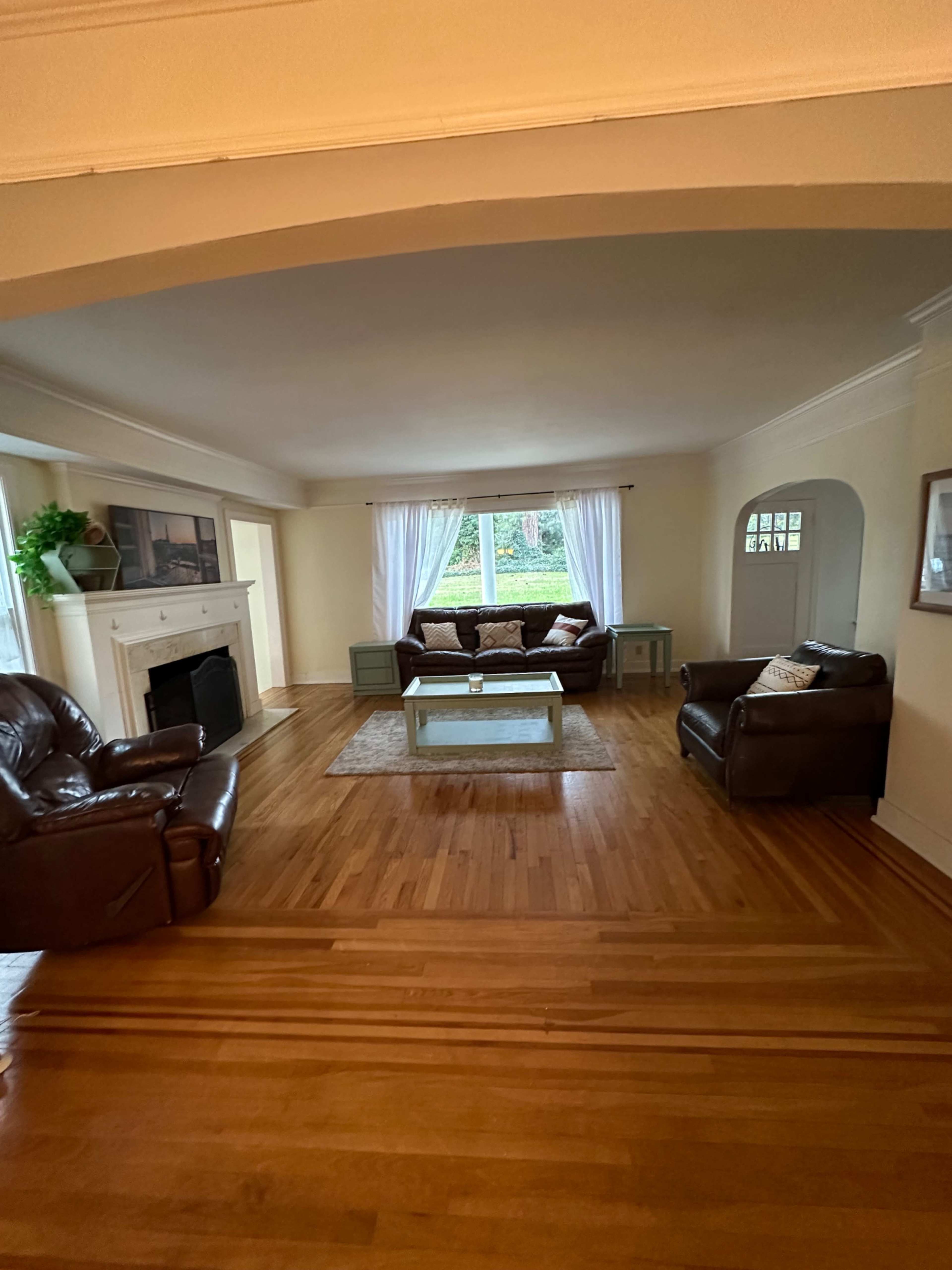 The living room features two leather sofas, a coffee table, and a fireplace, with large windows allowing natural light to enter.