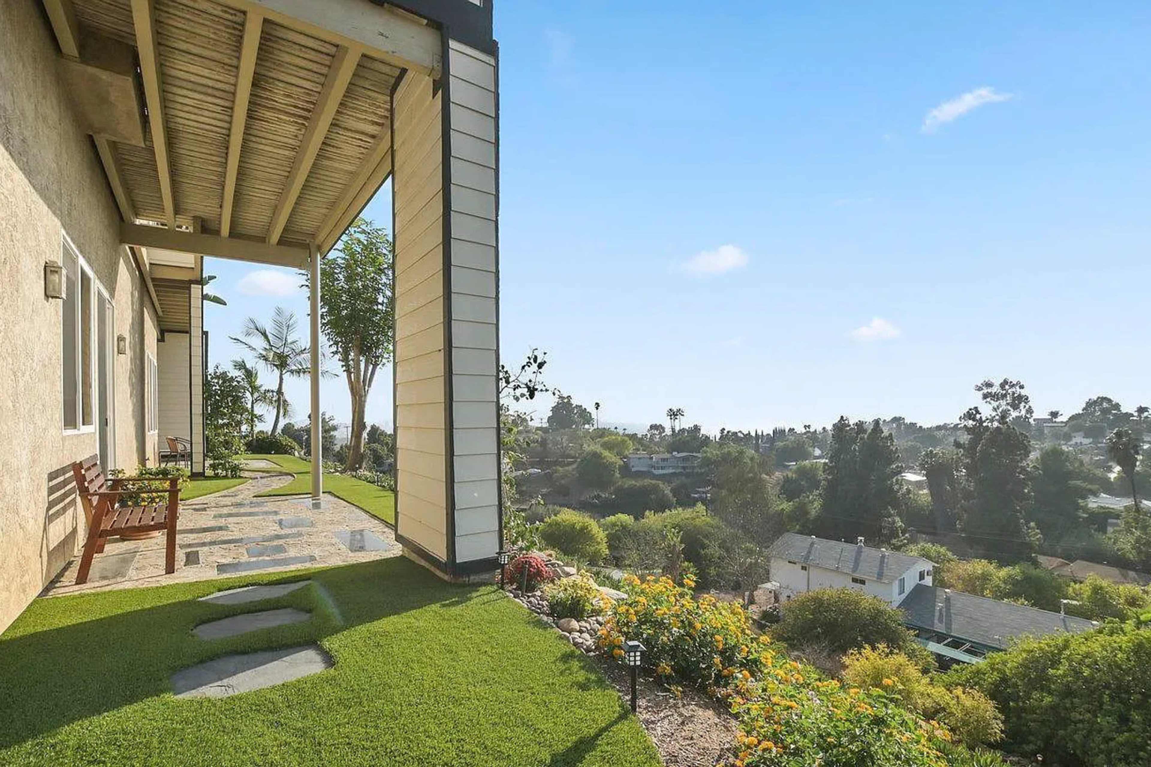 A landscaped outdoor area with a stone pathway and a view of a neighboring neighborhood under a clear blue sky.