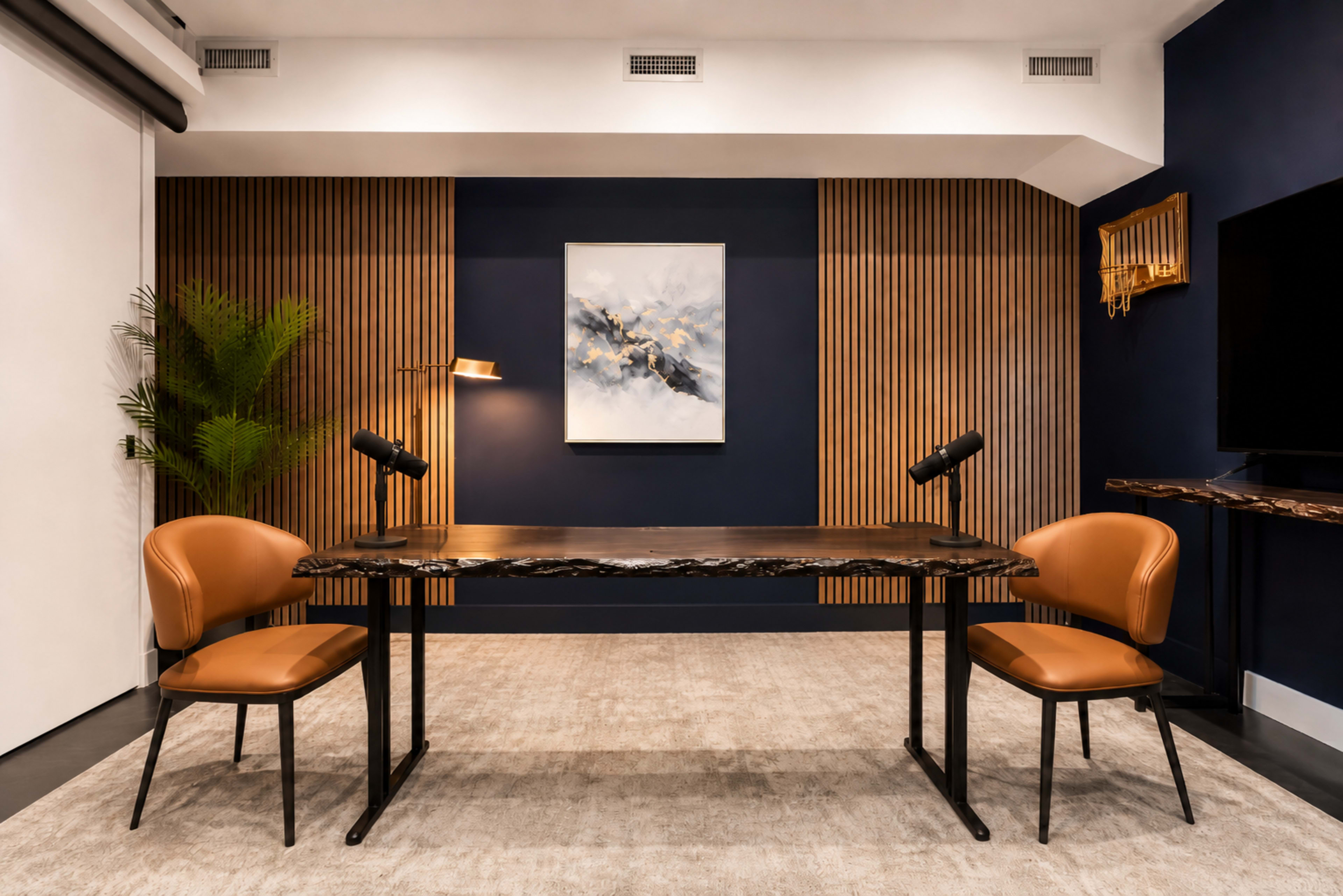 A modern office space features a wooden table with two brown chairs, flanked by a wall with wood paneling and a blue accent wall, along with a piece of abstract art.