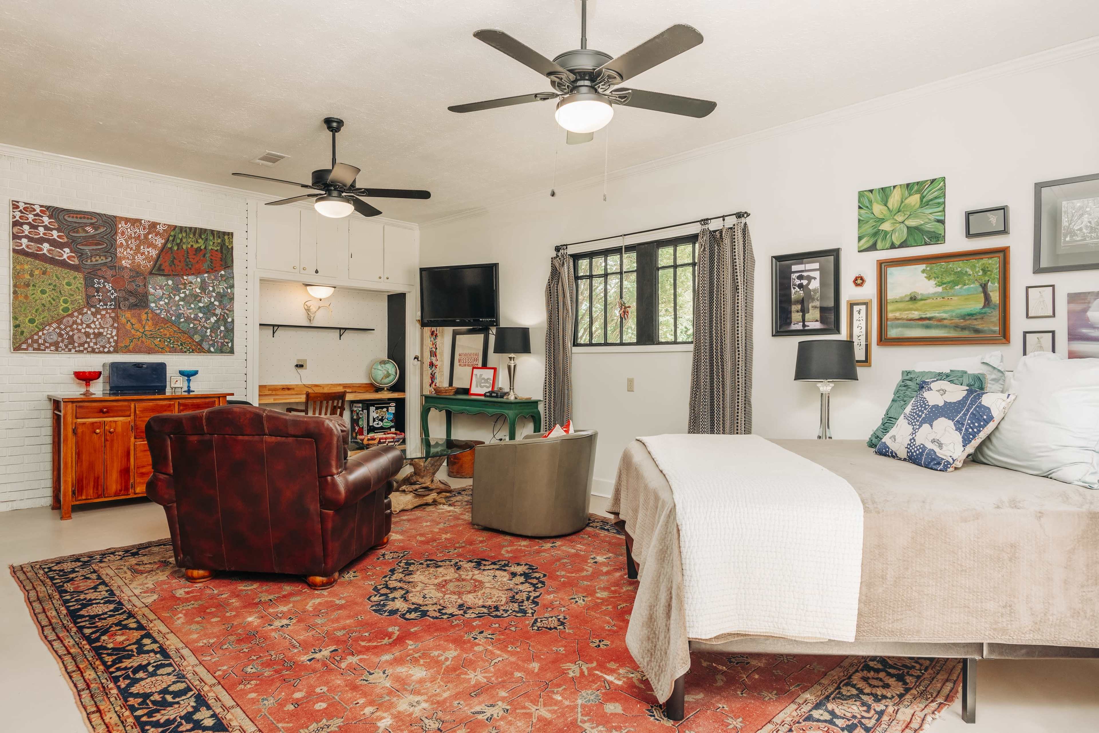The room features a bed, two ceiling fans, a seating area with a leather chair, and various artworks on the walls.