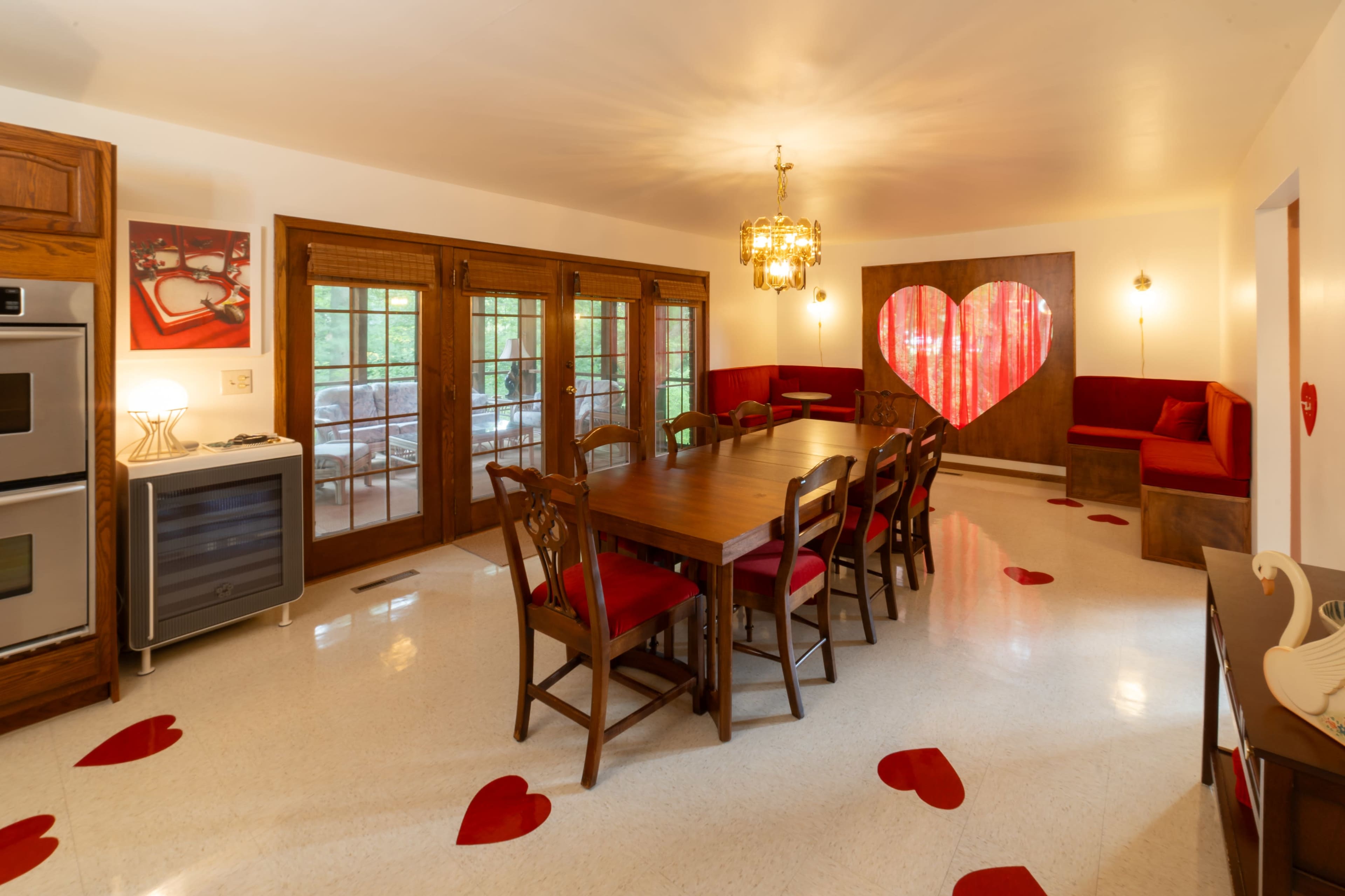 The kitchen features a large dining table surrounded by wooden chairs, with a heart-shaped decor element and heart designs on the floor.