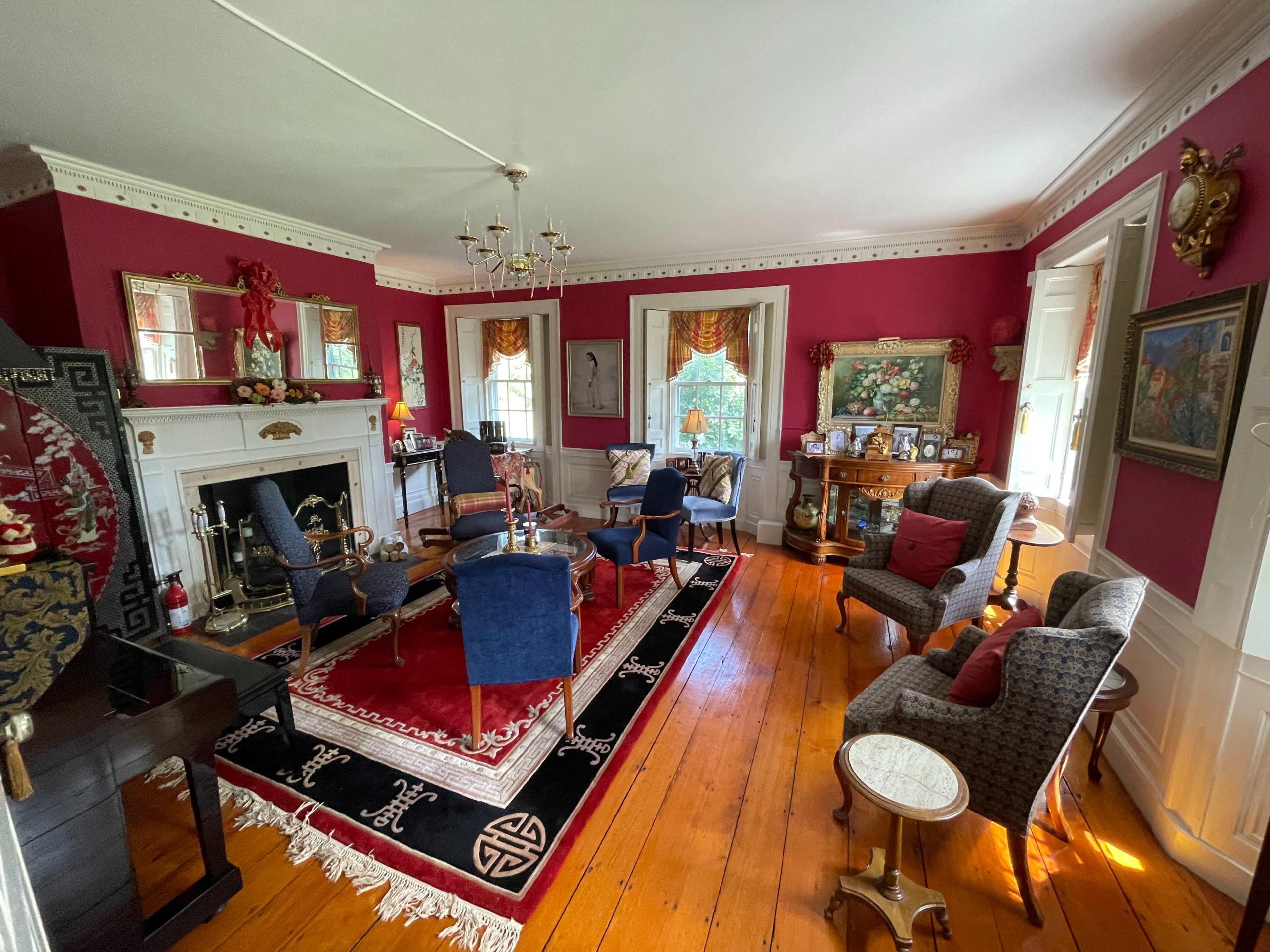 The room features hardwood floors, a large red rug, and several seating arrangements with chairs and a sofa, creating a cozy sitting area.