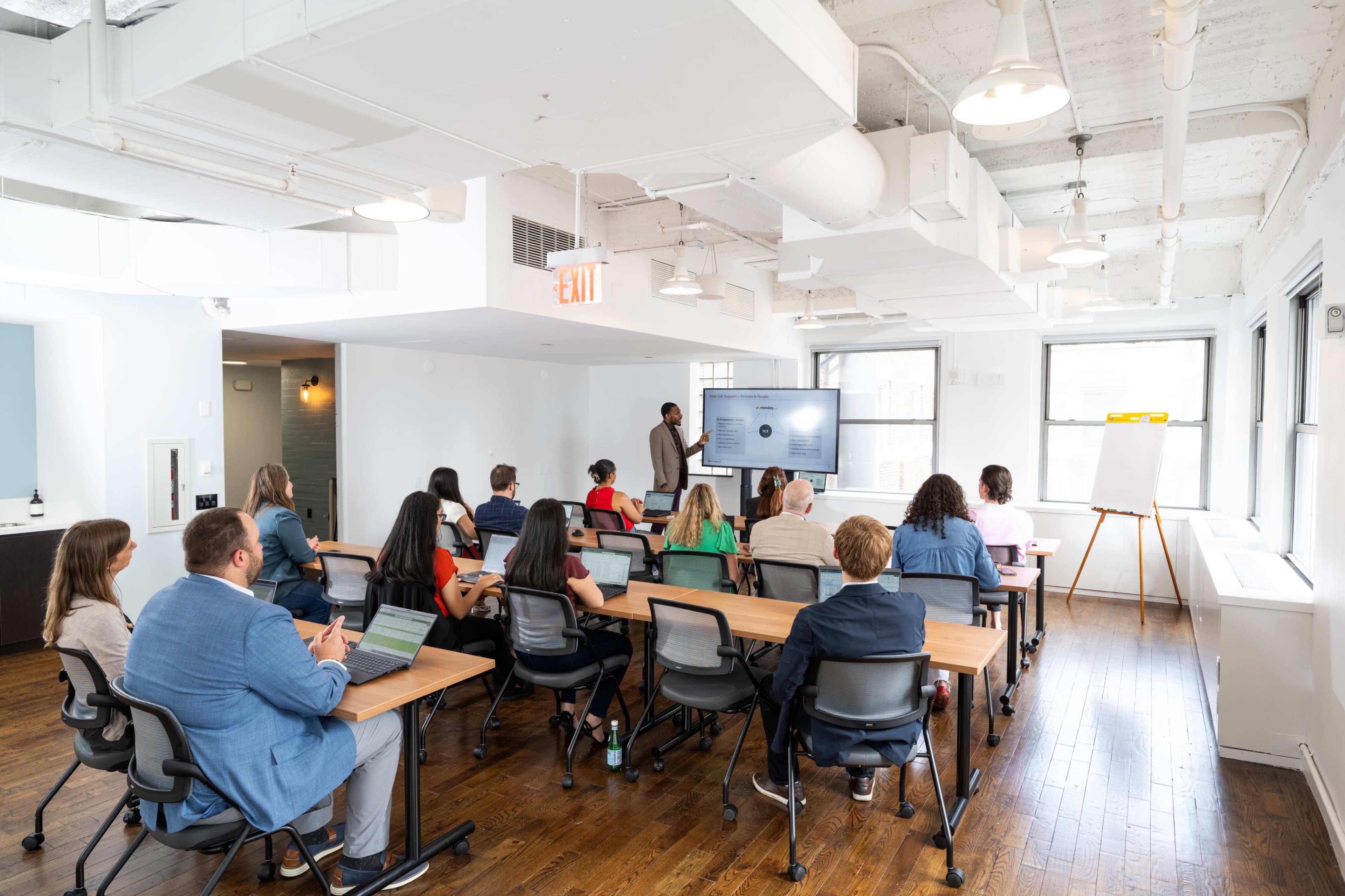 A group of people are seated in a modern conference room, attentively watching a presentation displayed on a large screen.