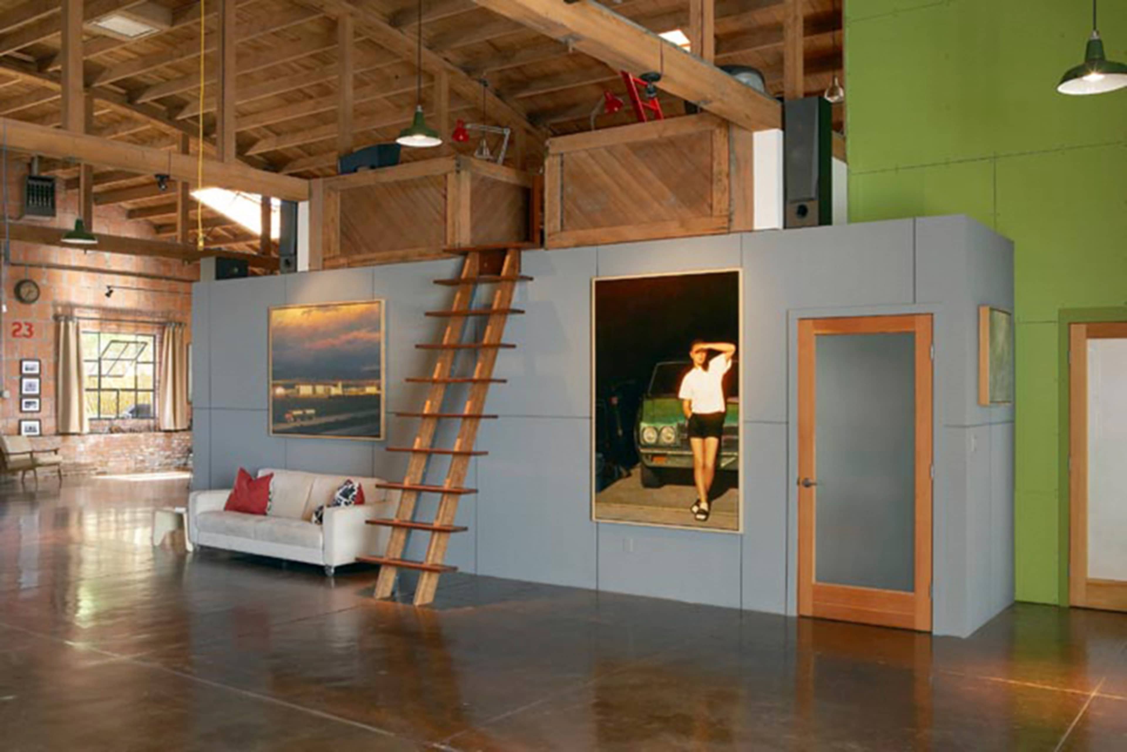 A loft-style interior with a wooden ceiling, a ladder leading to a raised area, and colorful walls featuring large framed artworks.