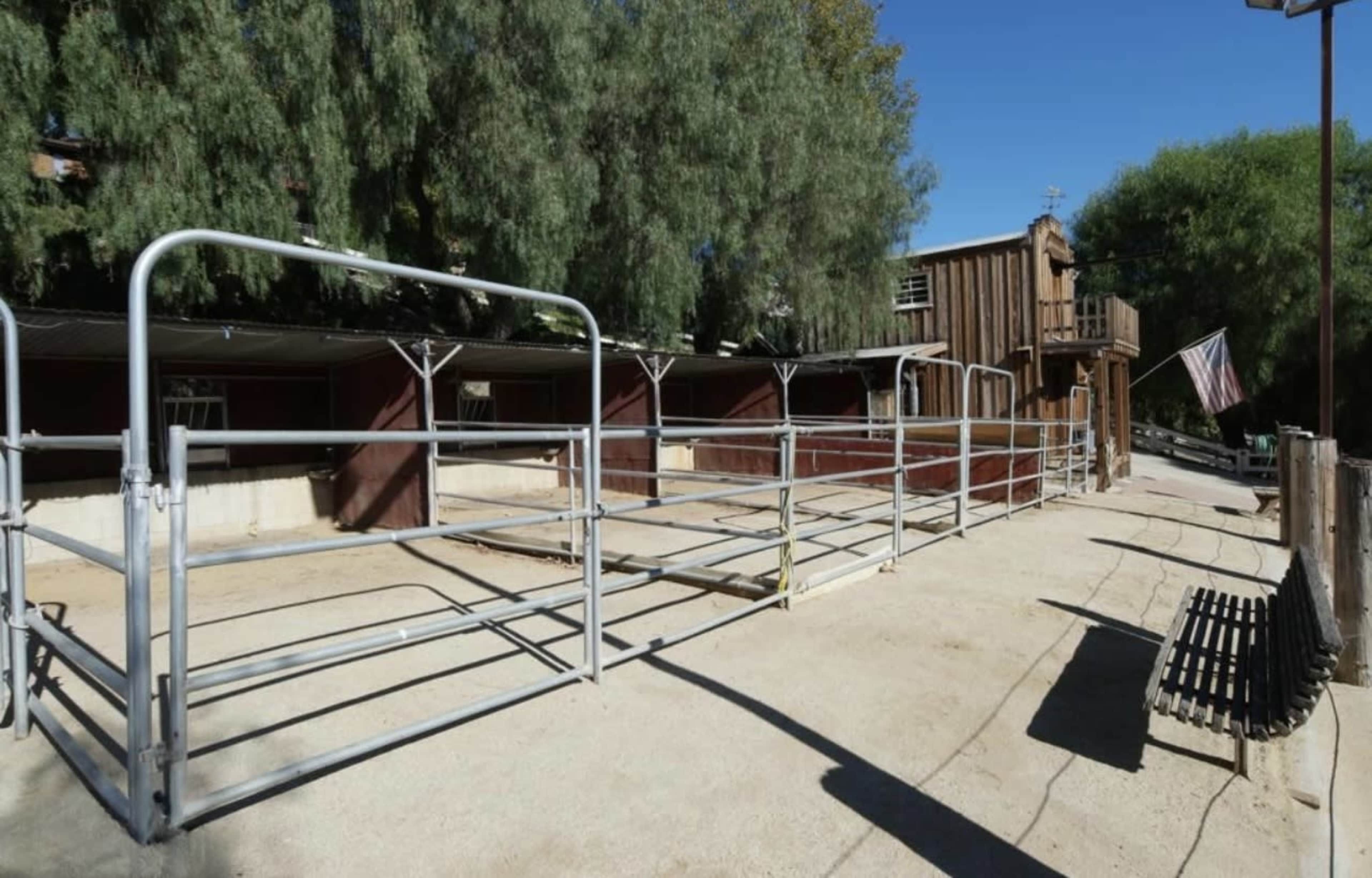 A fenced corral area next to a wooden structure, with a bench nearby under a clear blue sky.