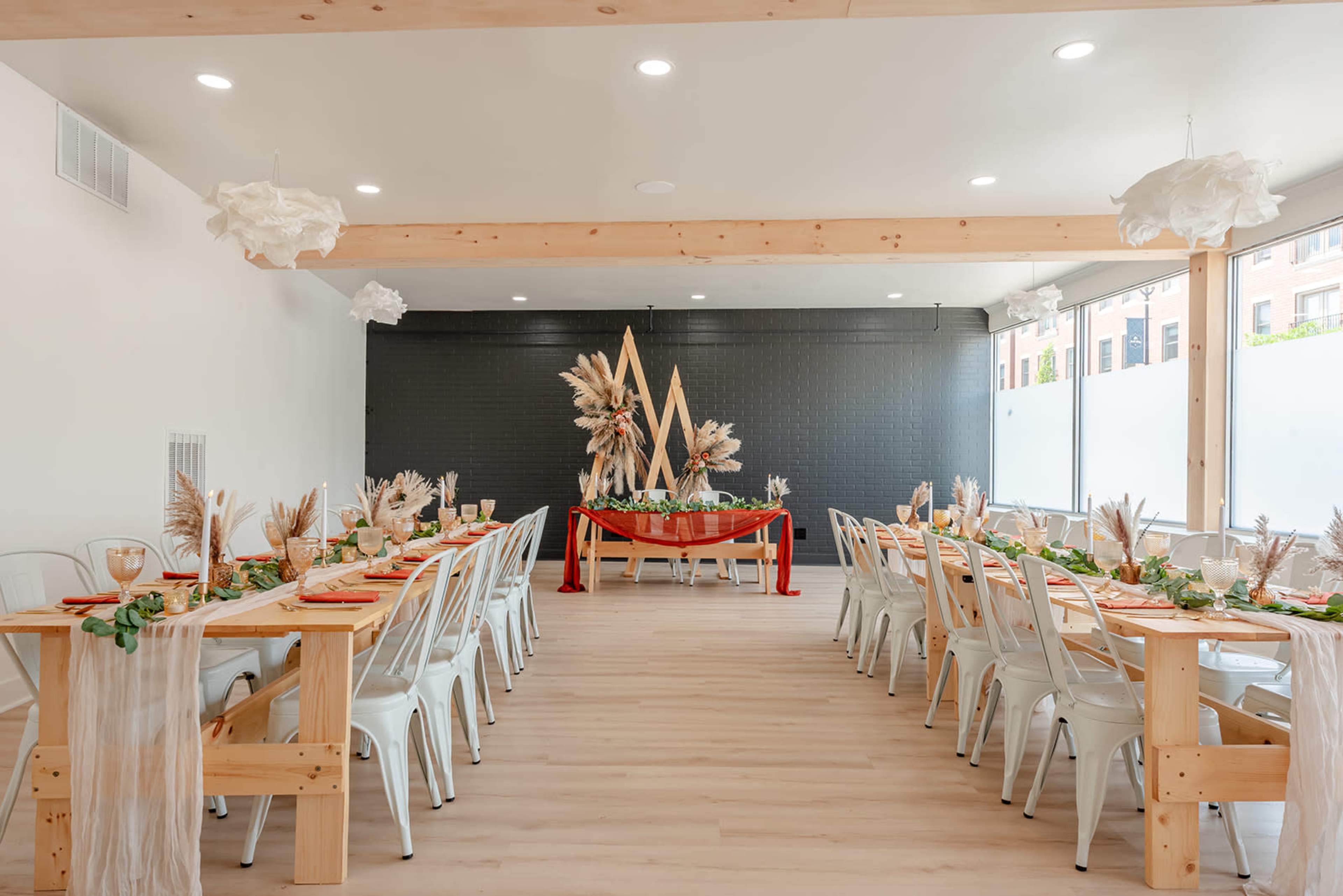 A light-filled dining room features long wooden tables set with decorative centerpieces and elegant table settings.