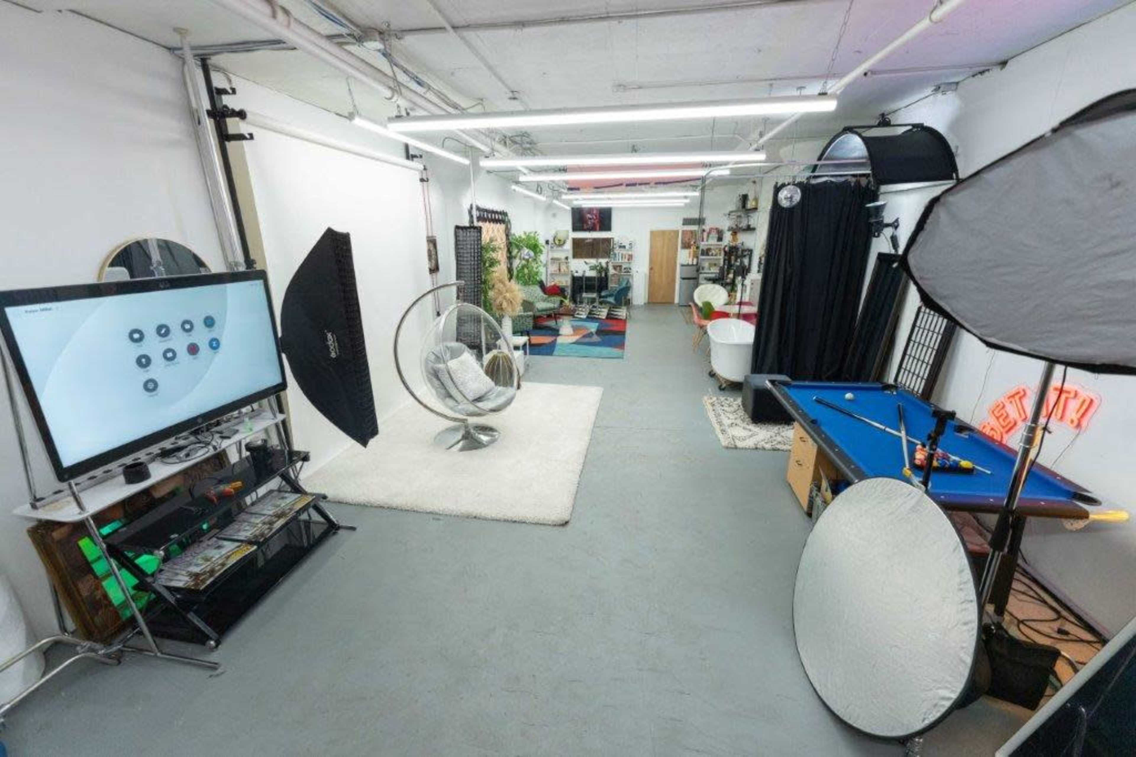 A photo studio setup featuring a television, a round chair, lighting equipment, a pool table, and various decorative elements.