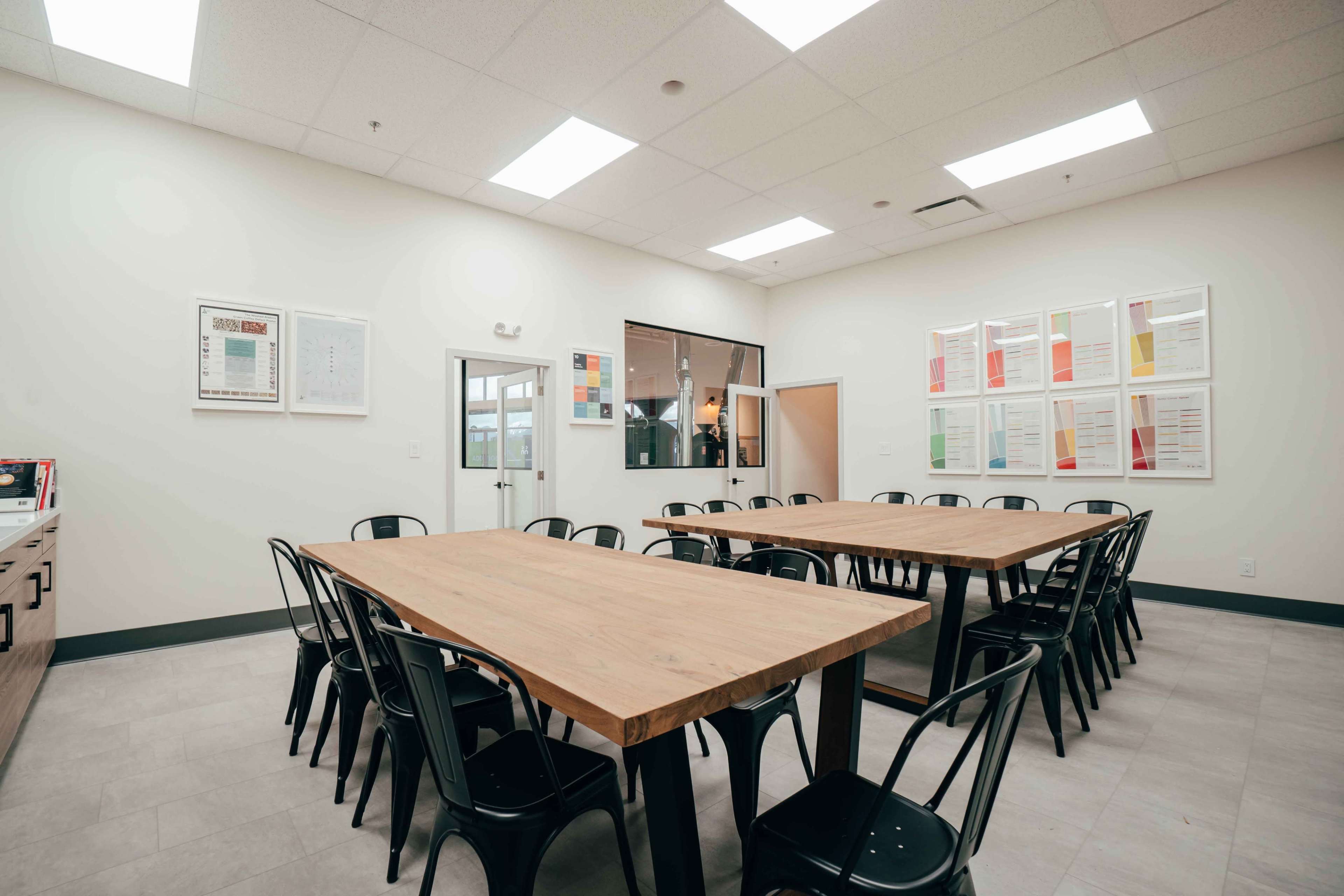A spacious meeting room equipped with two large wooden tables arranged for group seating and several framed documents on the walls.