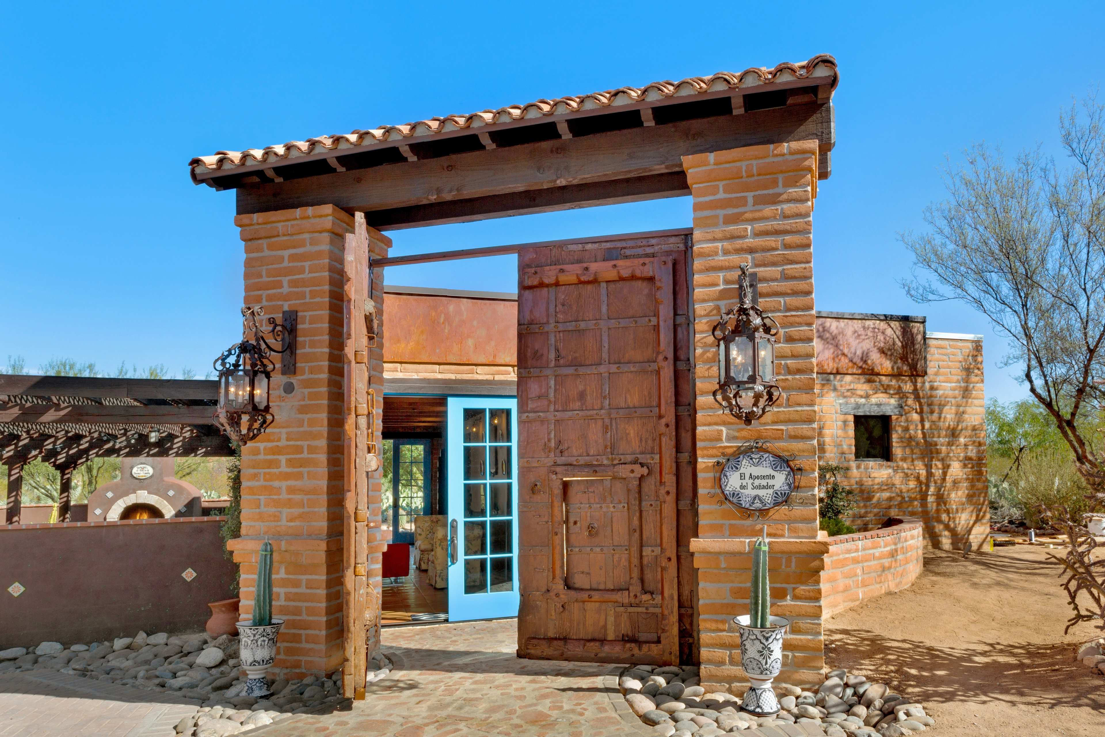 A large wooden gate with intricate carvings stands open, revealing a southwestern-style courtyard adorned with stone and colorful architecture.