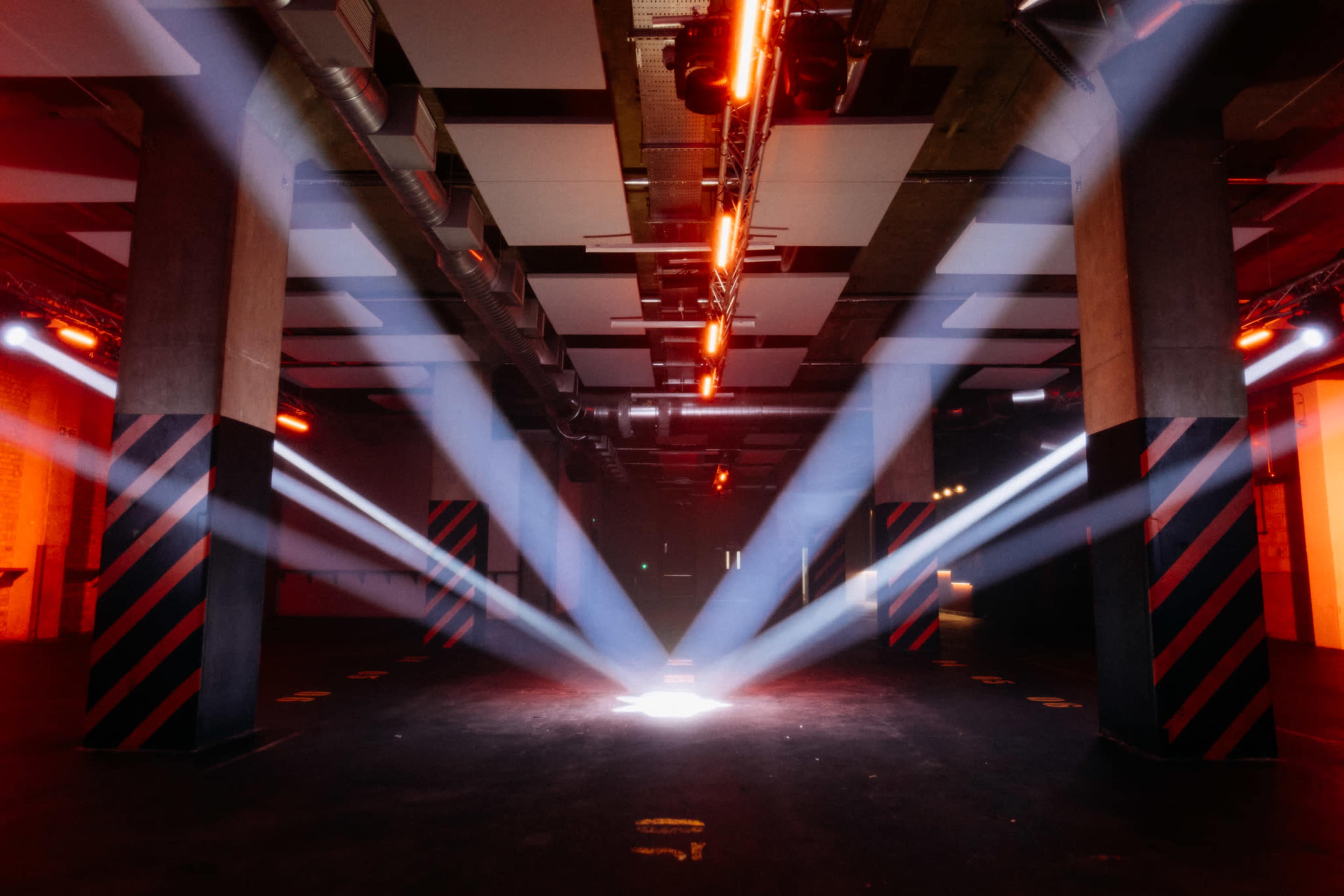 A large, dimly lit industrial space featuring beams of light shining down from the ceiling onto a central area.