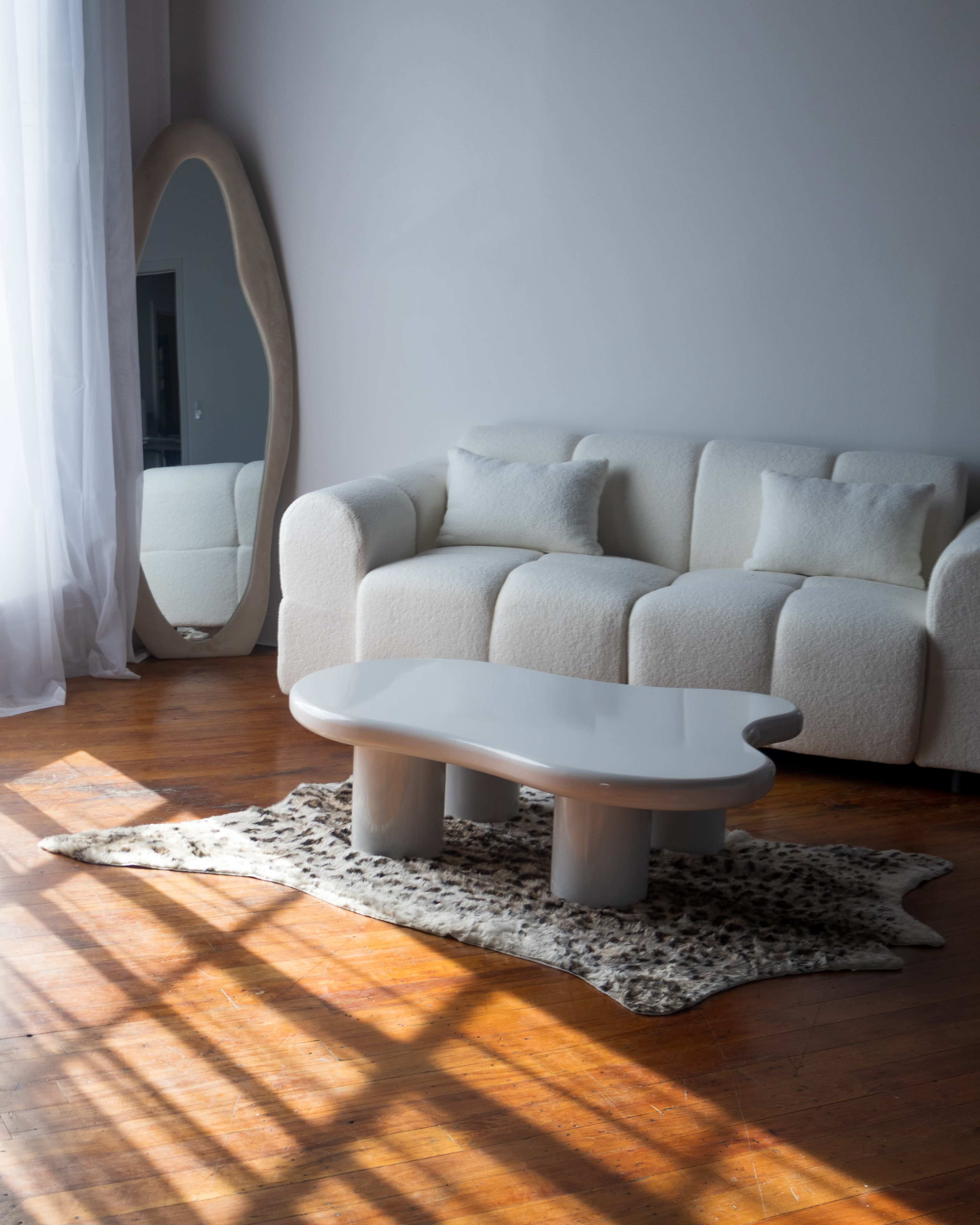 A white upholstered sofa with three cushions faces a coffee table on a patterned rug in a well-lit room with wooden floors.