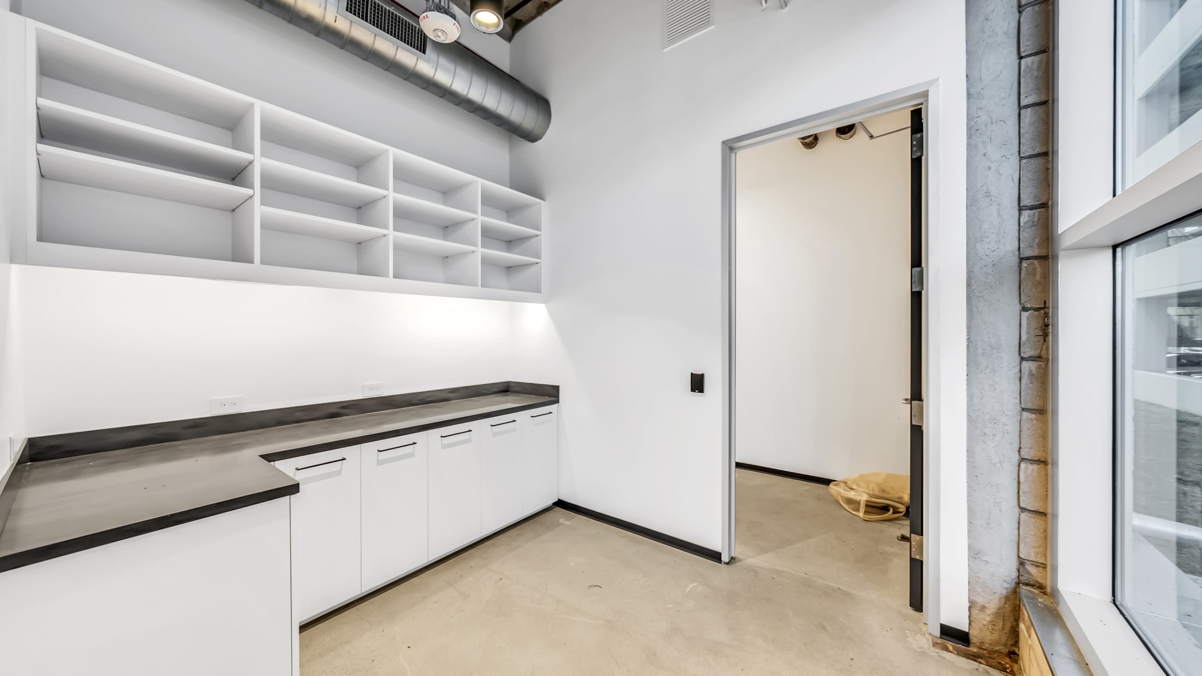 A modern empty room with white walls, concrete flooring, and built-in shelves, along with a door leading to another space.