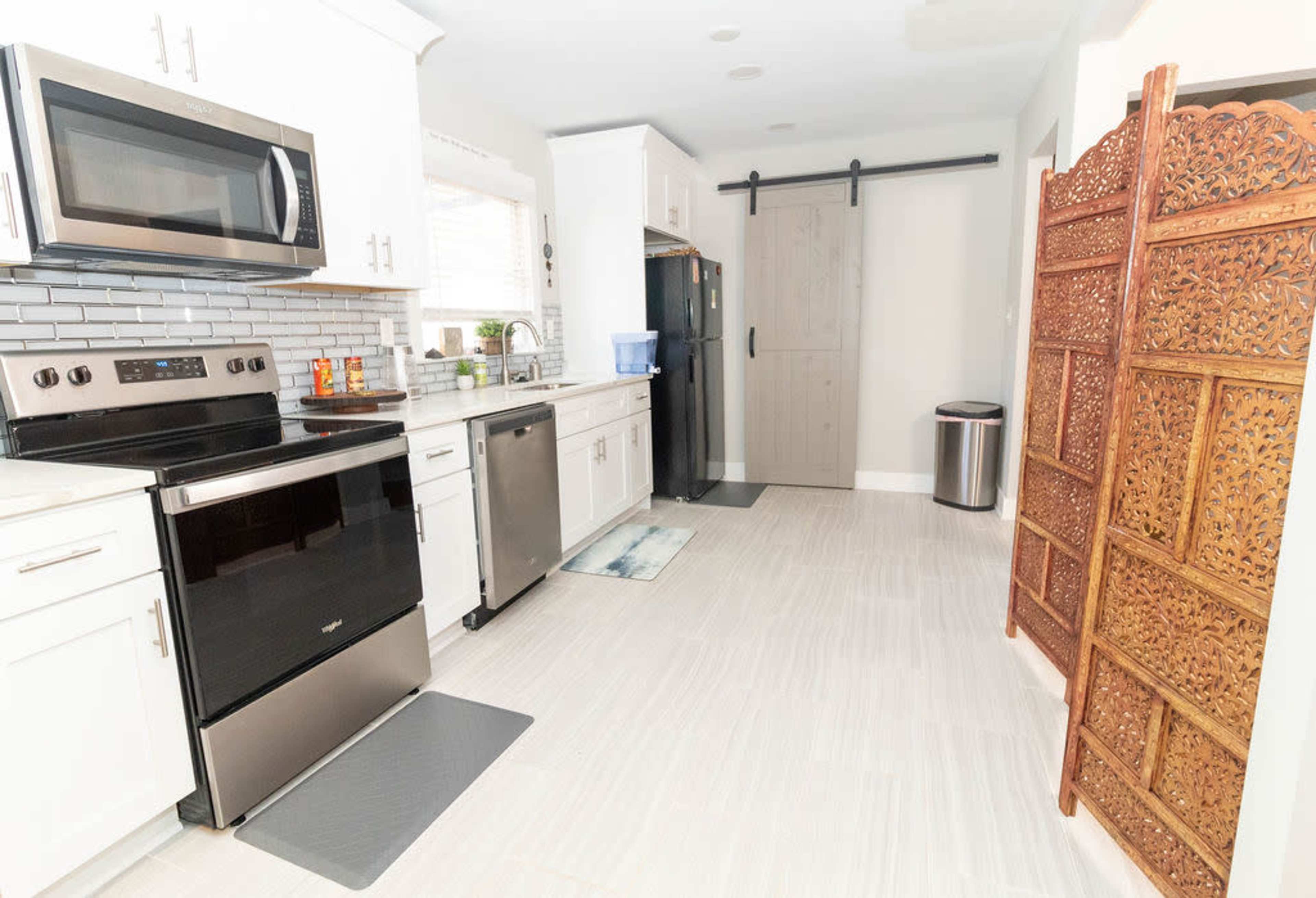 The image shows a kitchen with white cabinets, stainless steel appliances, and a decorative wooden room divider near the entrance.