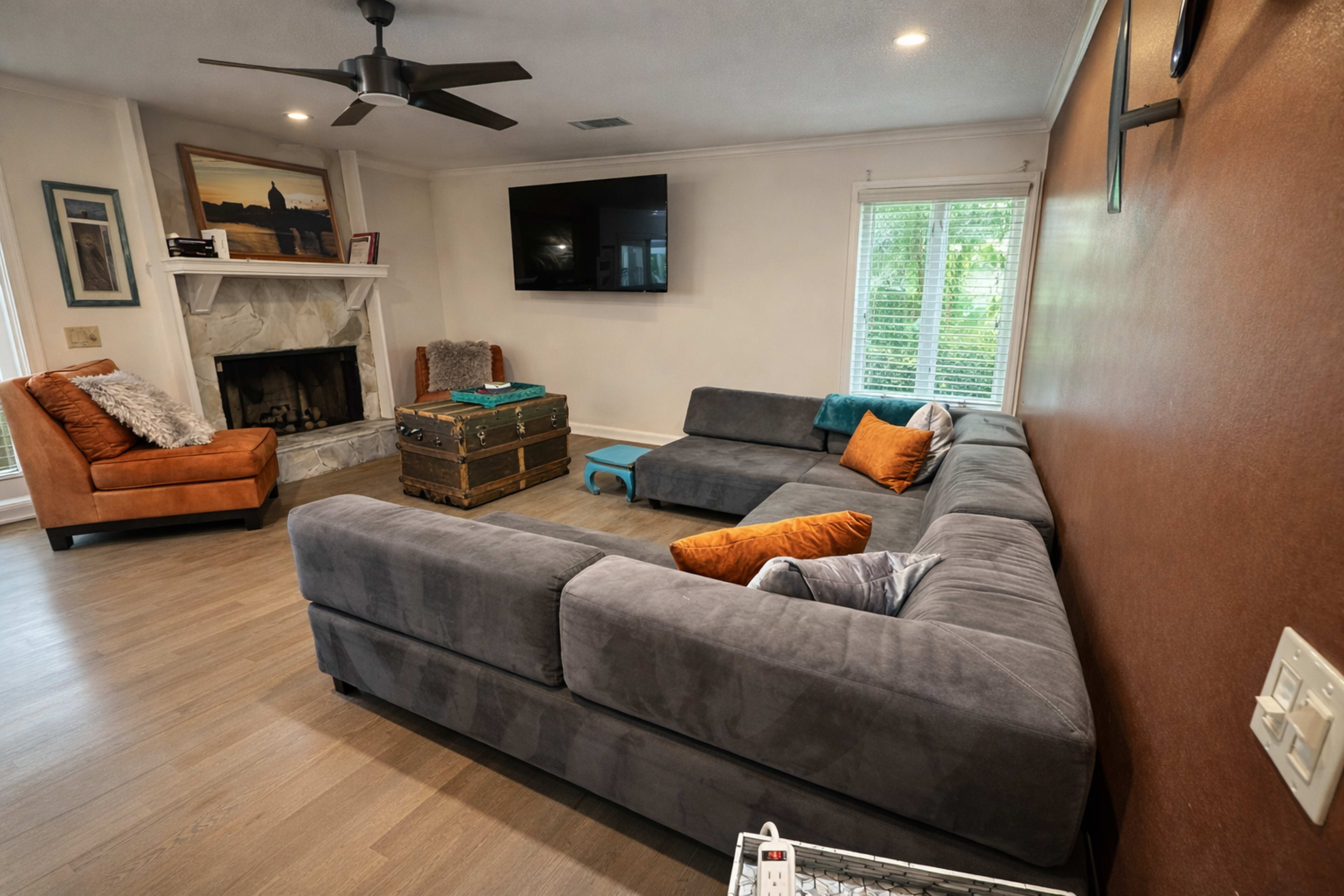 The living room features a gray sectional sofa, an orange accent chair, a wooden coffee table, and a fireplace with a television mounted on the wall.