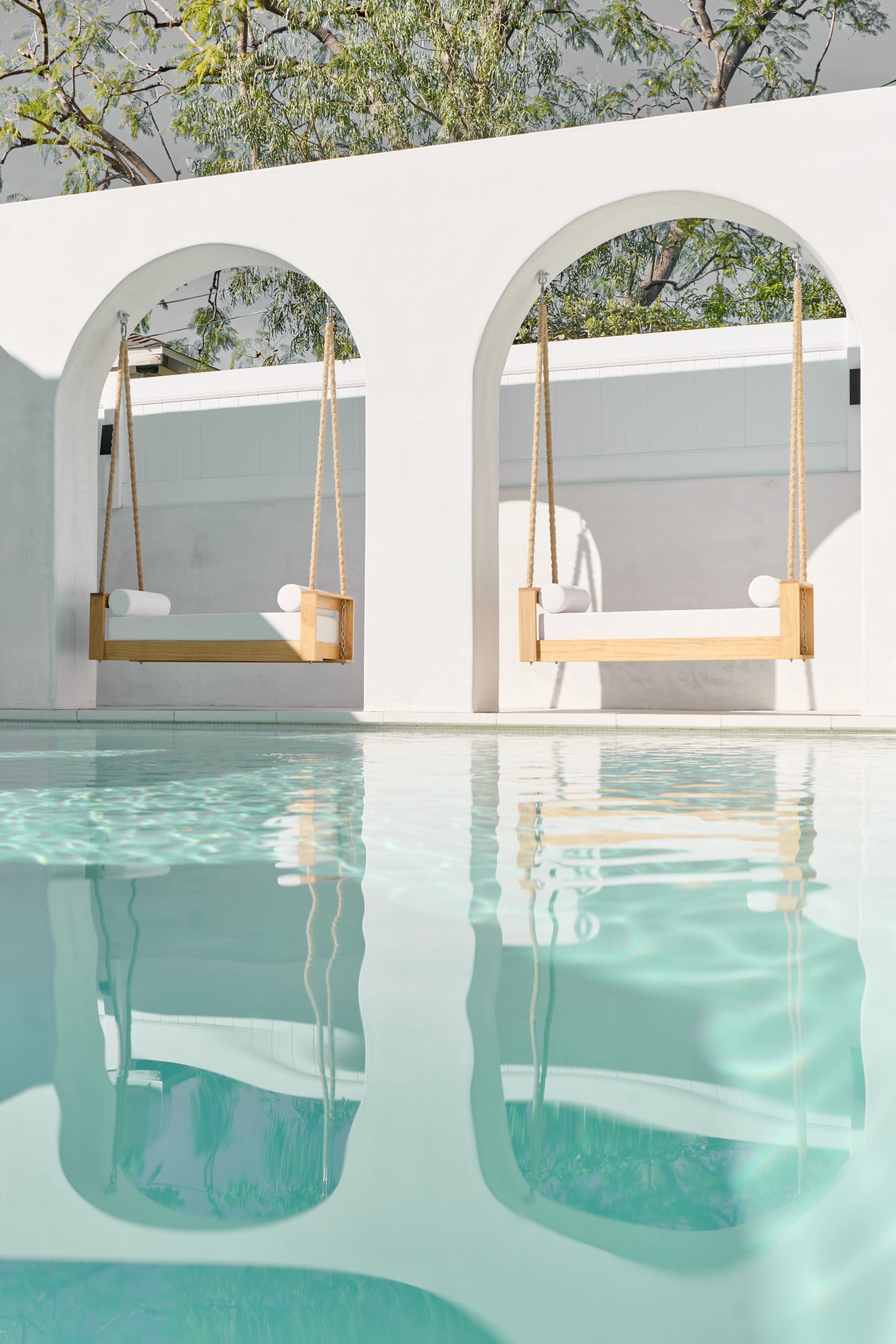 The image features a serene pool area with two wooden swings suspended in white arches, reflecting in the clear water.