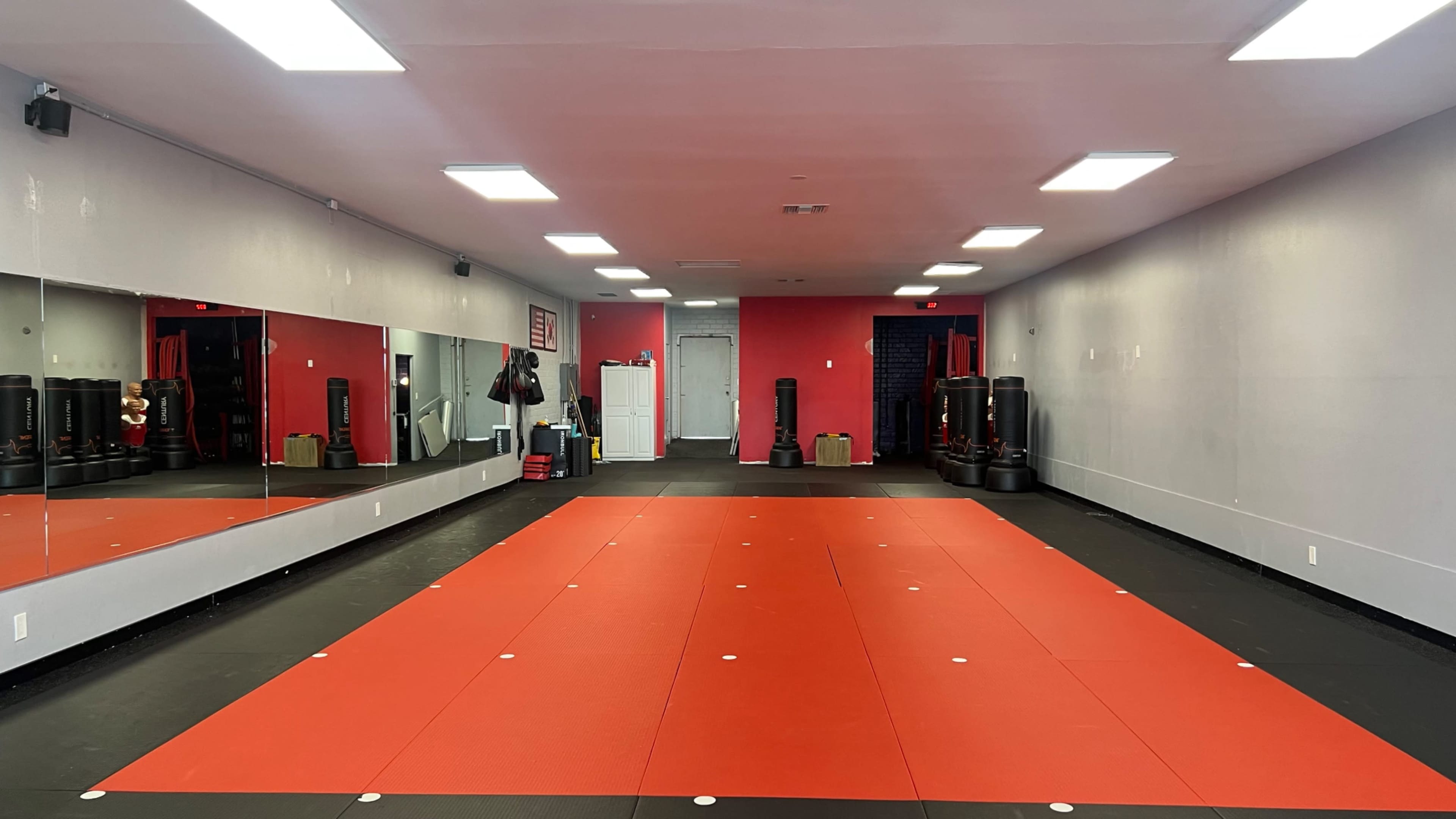 A martial arts training room featuring red and black flooring, a large mirror, and various training equipment against the walls.