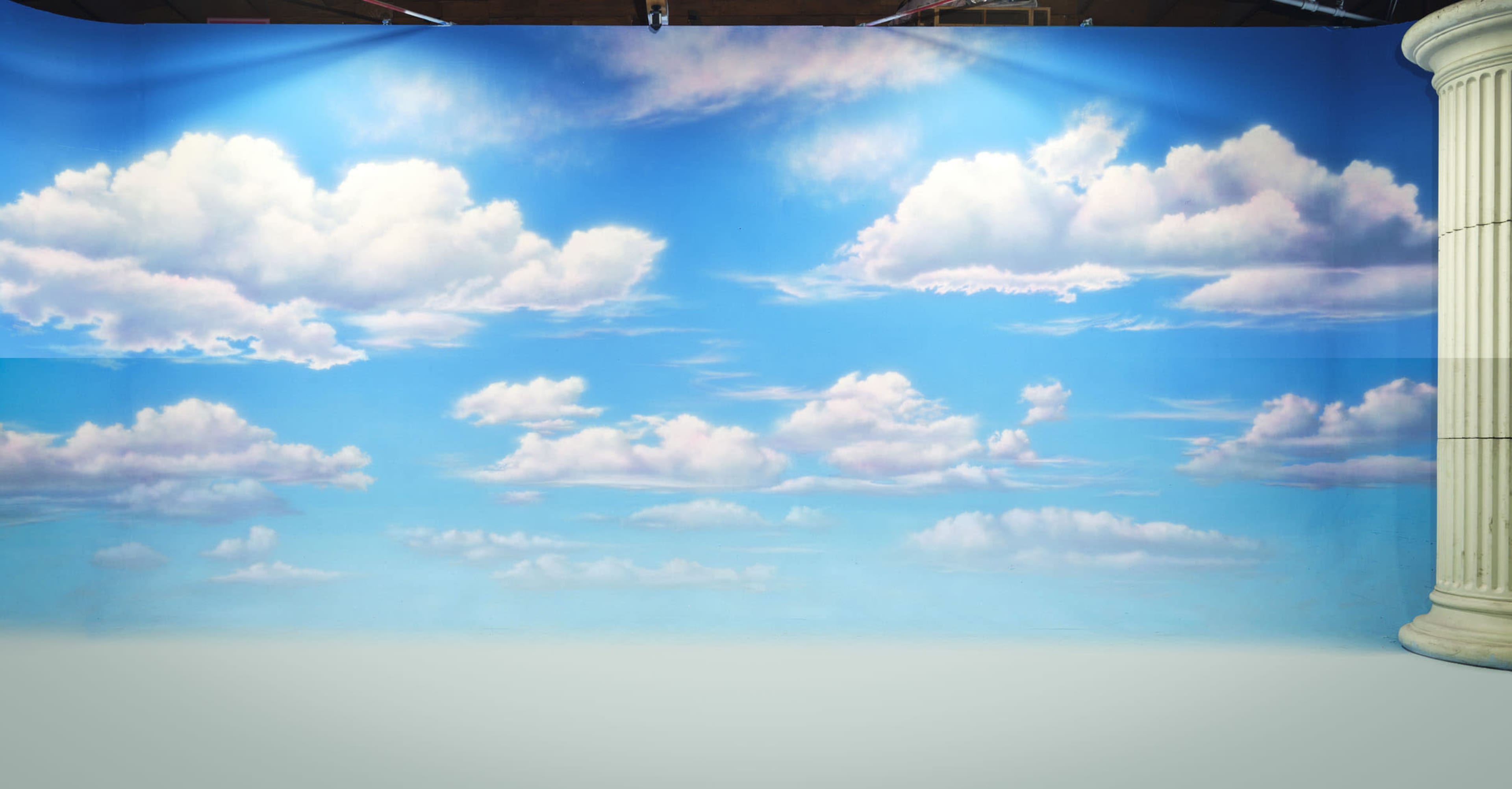 The image features a painted backdrop of a blue sky adorned with fluffy white clouds.
