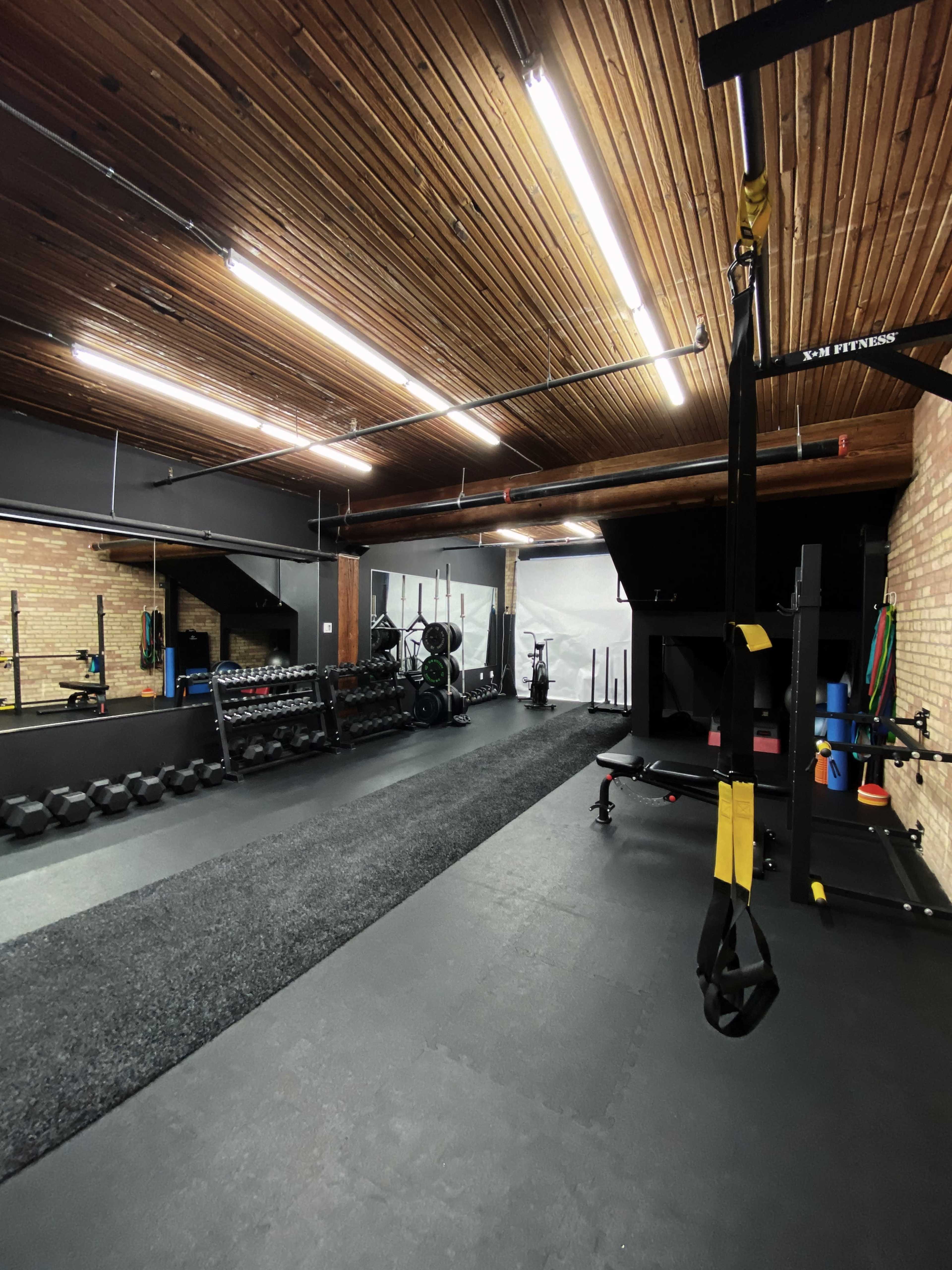 A spacious gym with wooden ceilings, equipped with free weights, resistance bands, and training machines.